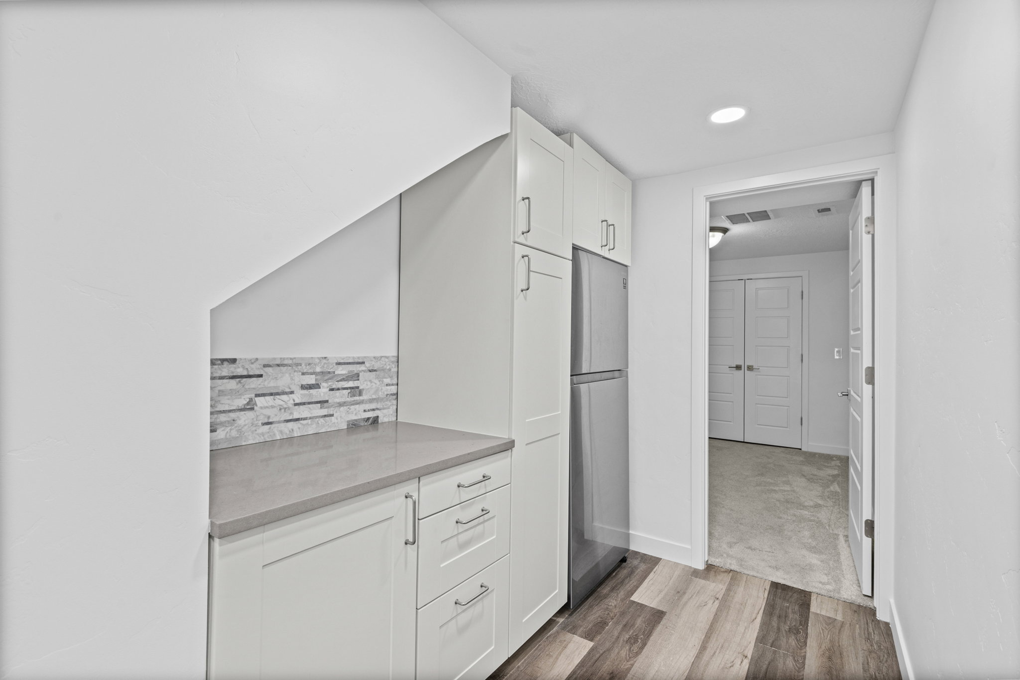 Compact kitchen area featuring white cabinetry, a stainless steel refrigerator, a light gray countertop, and a stacked stone backsplash