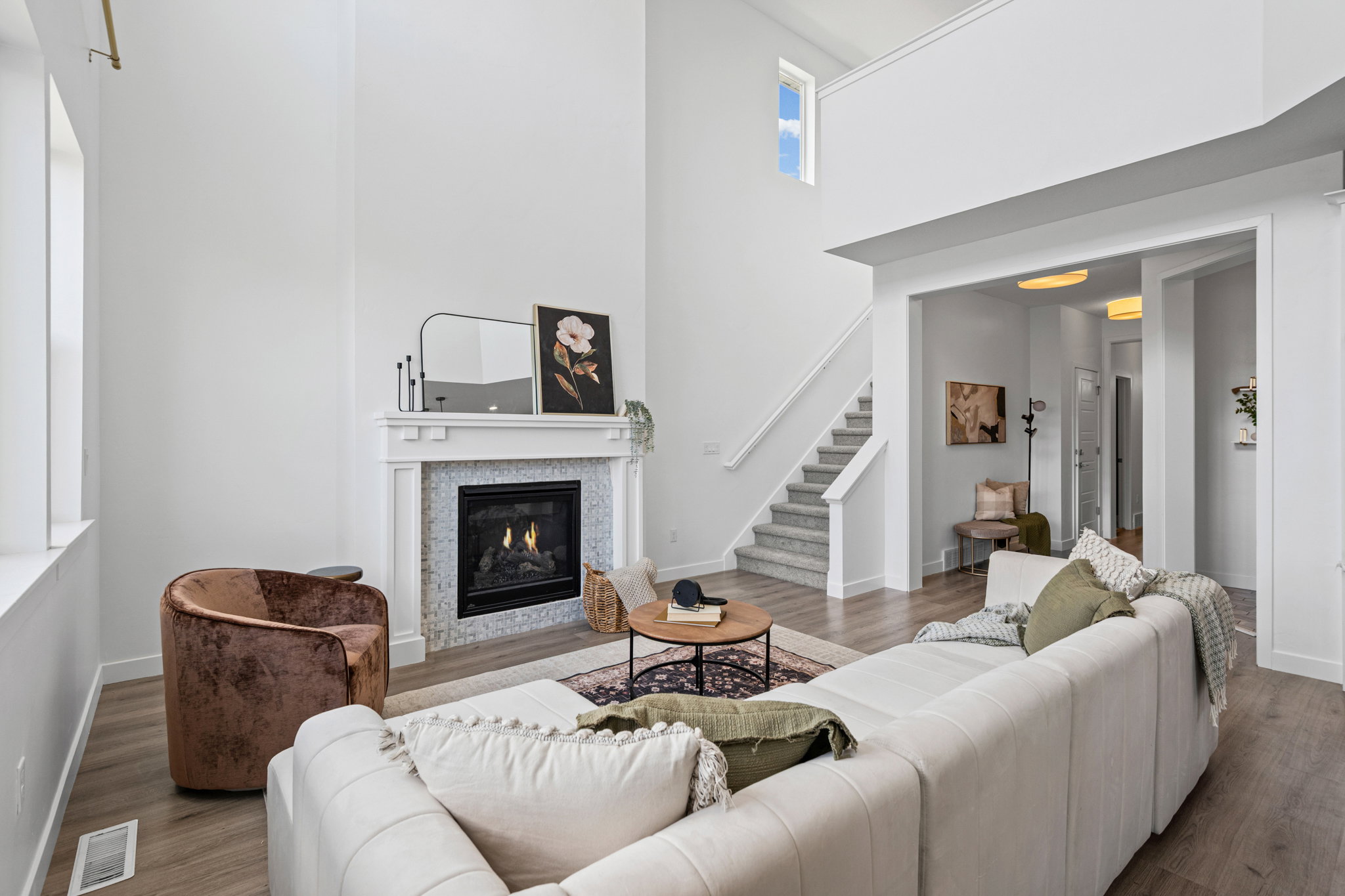 Vaulted ceiling living area featuring a fireplace with a white mantel and mosaic tile surround, wood-finish flooring, and natural light from a large window