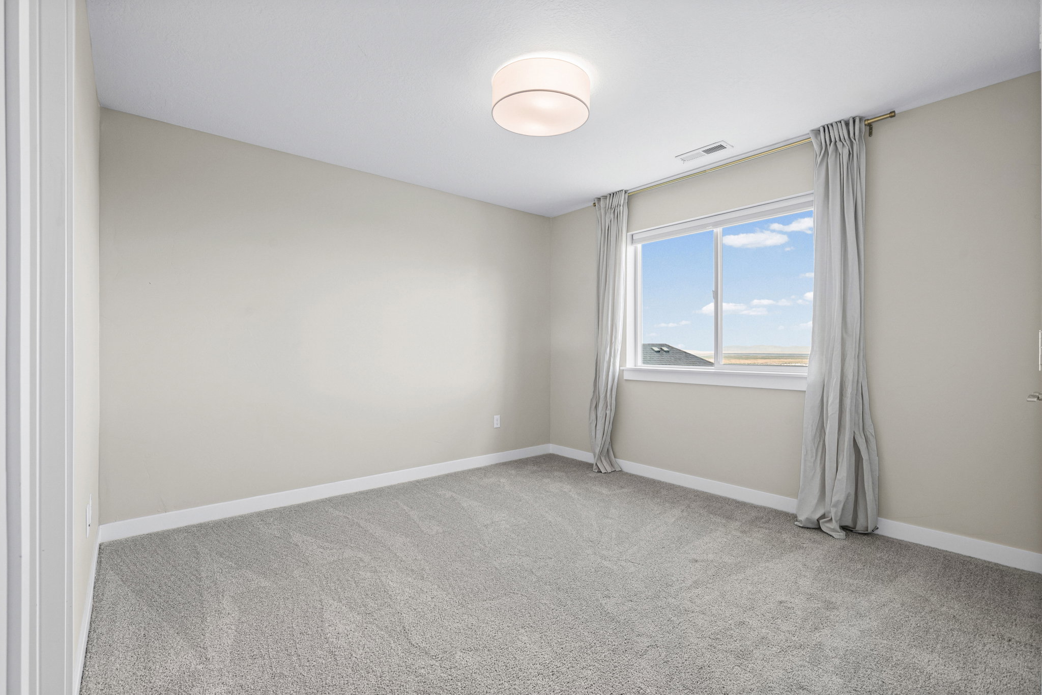 Neutral-toned room featuring a large window with distant scenery, light gray wall-to-wall carpeting, white baseboards, and a contemporary ceiling light fixture