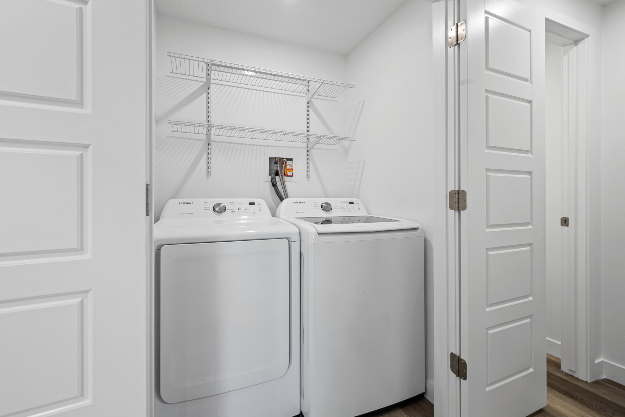 Dedicated laundry area featuring white walls, wood-finish flooring, two large appliances, and wire shelving