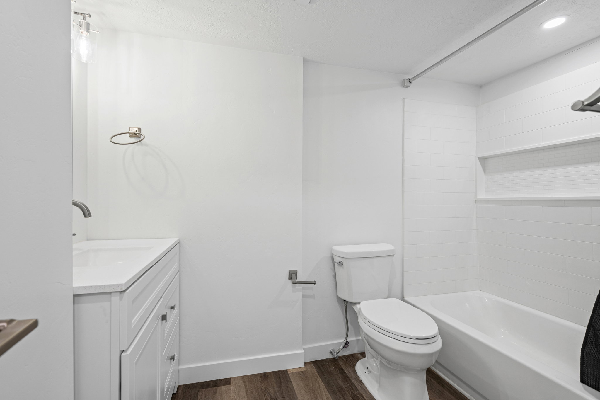 Bathroom featuring a white vanity with a solid surface countertop, a wall-mounted faucet, wood-finish flooring, a white toilet, and a bathtub with white subway tile surround