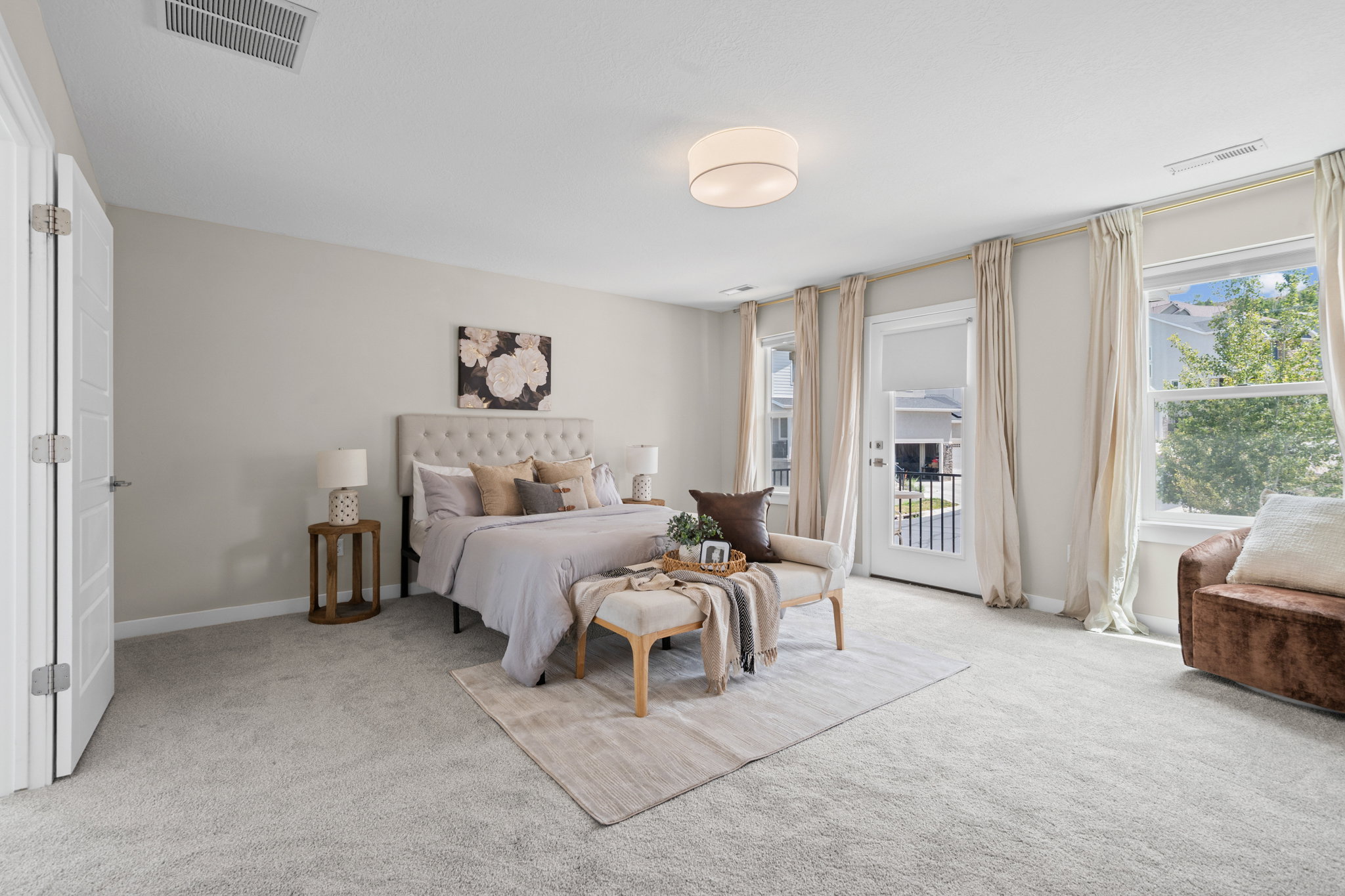 Spacious bedroom featuring light-colored carpet flooring, a ceiling-mounted light fixture, and a large window with a white frame
