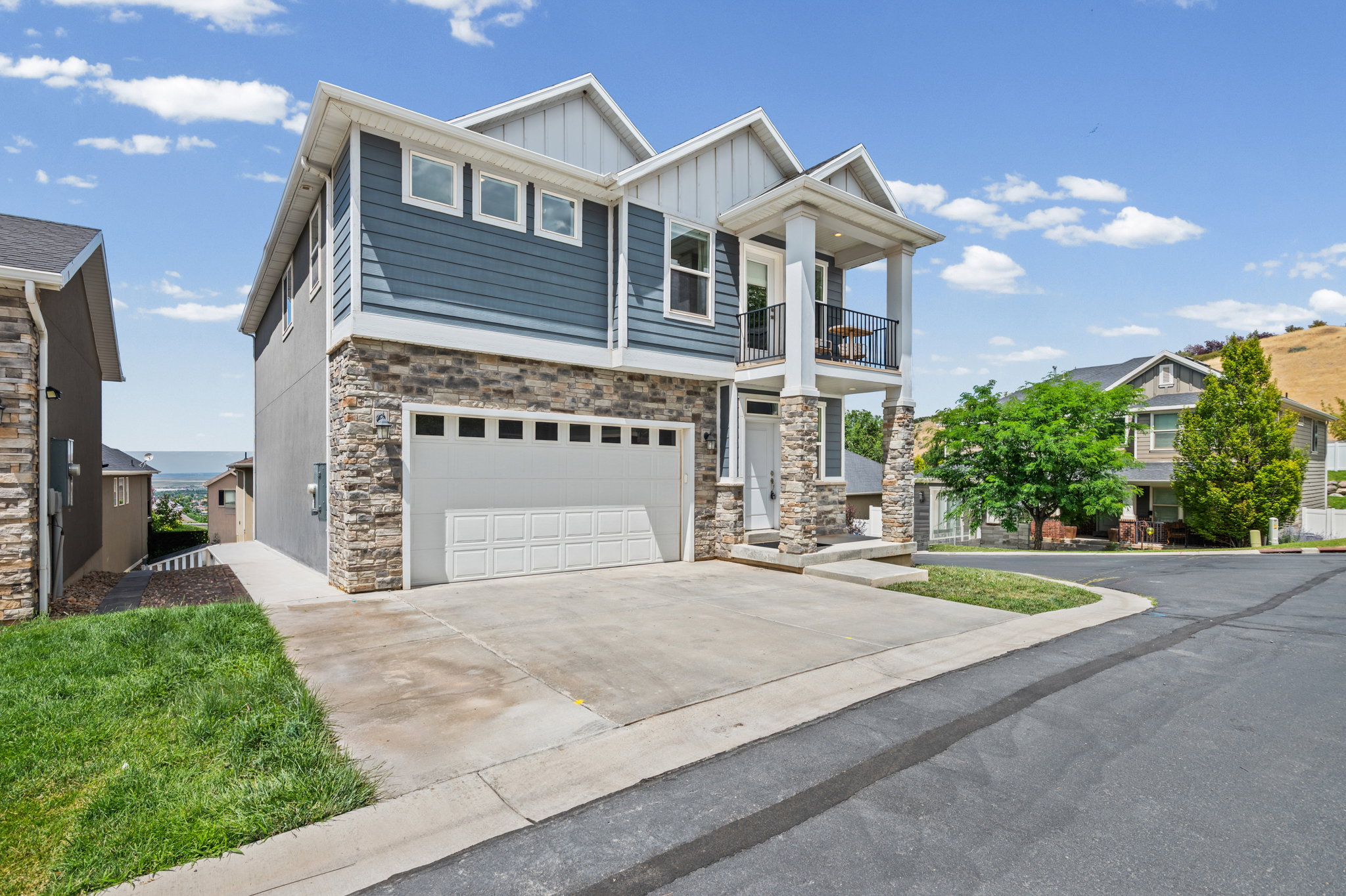 Contemporary residence featuring a two-car garage, stone veneer and horizontal siding façade, covered entry, and an upper-level balcony with metal railing