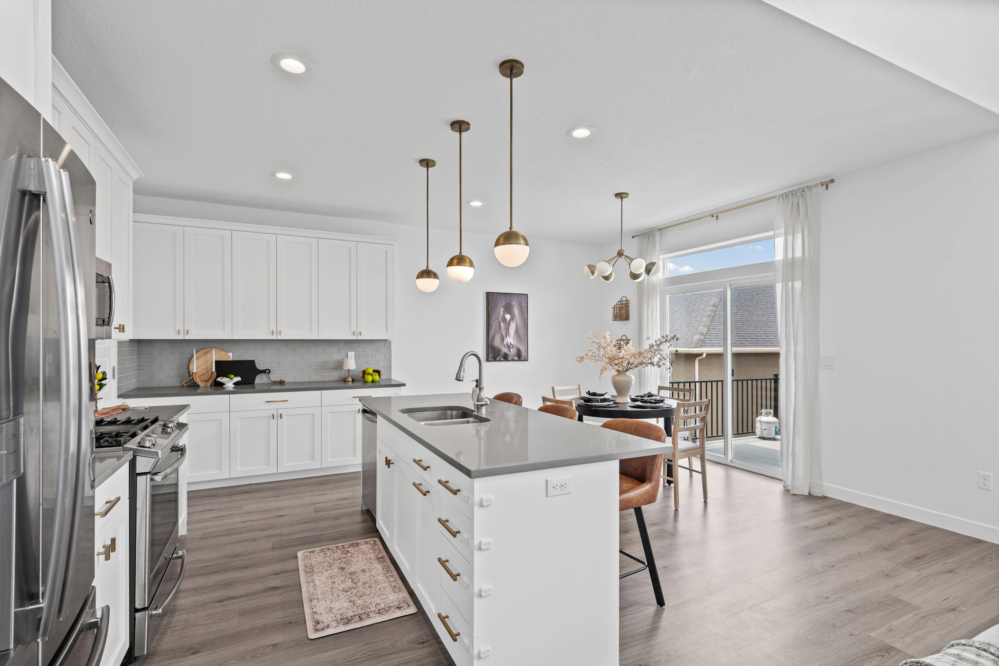 Modern kitchen featuring white cabinetry, stainless steel appliances, a center island with sink, quartz countertops, and wood-finish flooring