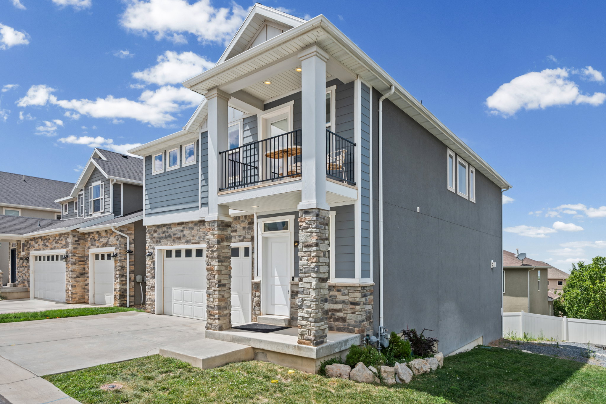 Contemporary multi-story exterior with stone veneer accents, light blue siding, and a white front door