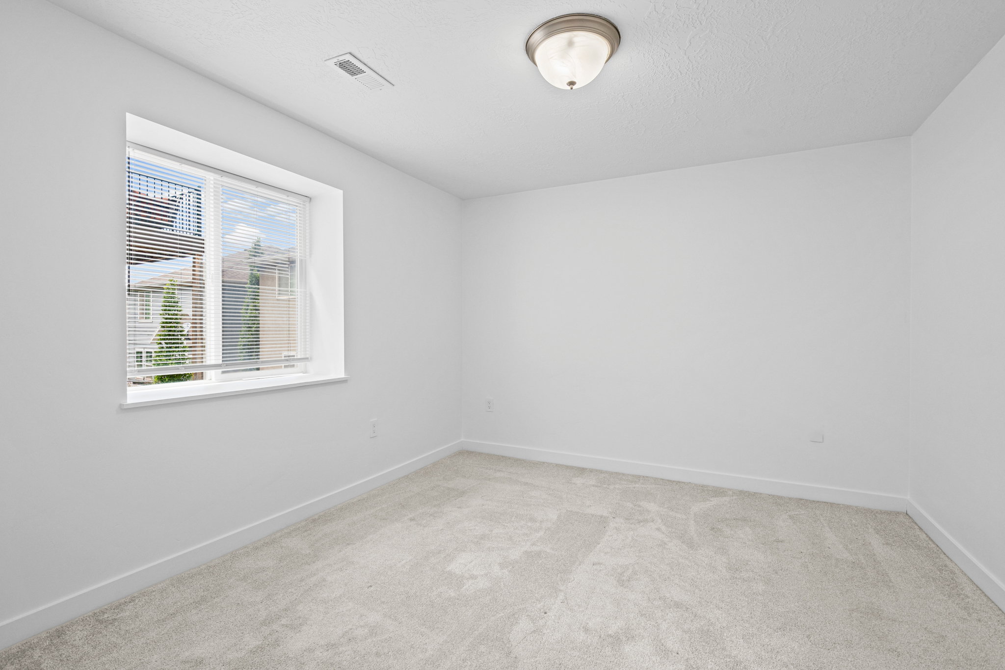 Bright room featuring light grey carpeting, white walls, and a single window with blinds