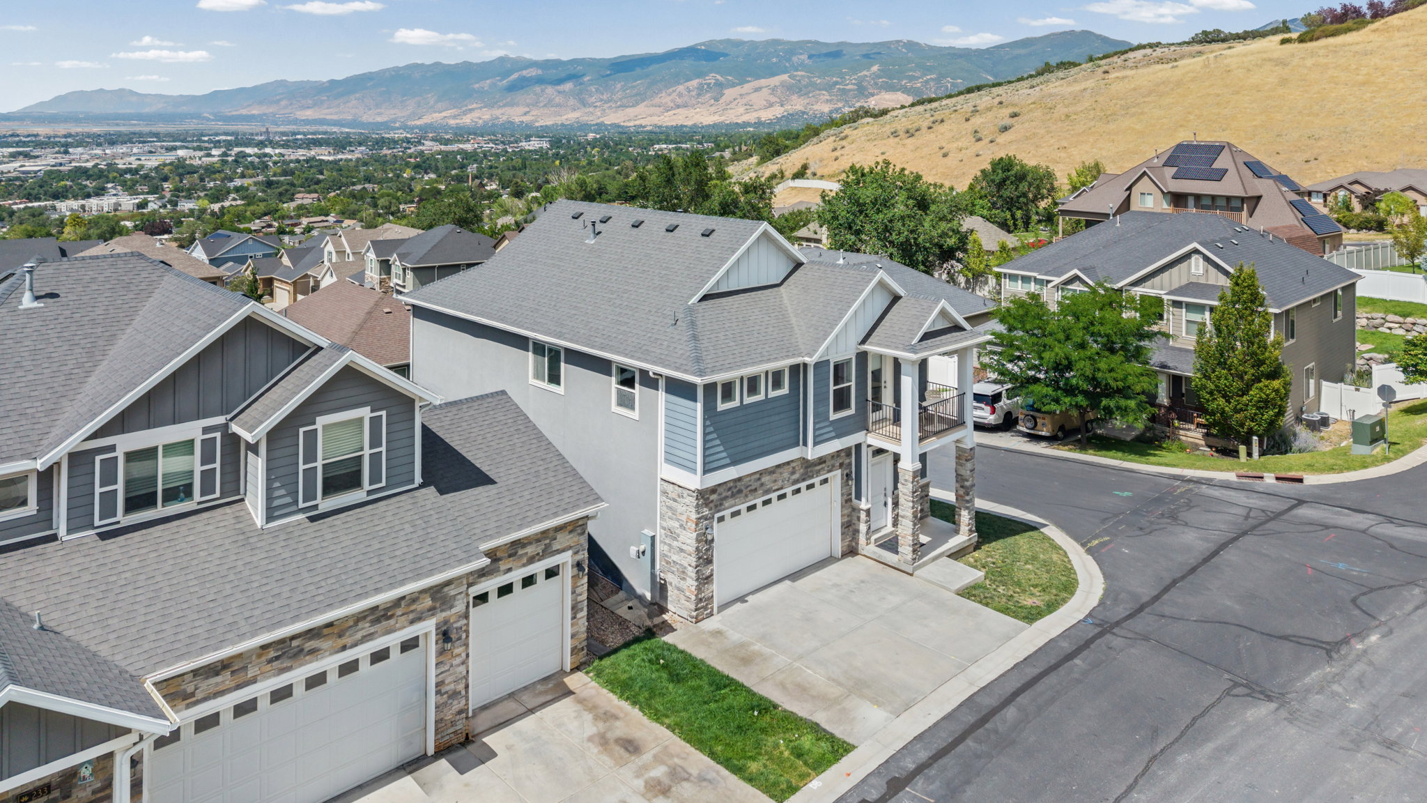 Contemporary multi-story residence featuring a two-car garage, stone and siding exterior, a second-story balcony, and a prominent gable roofline
