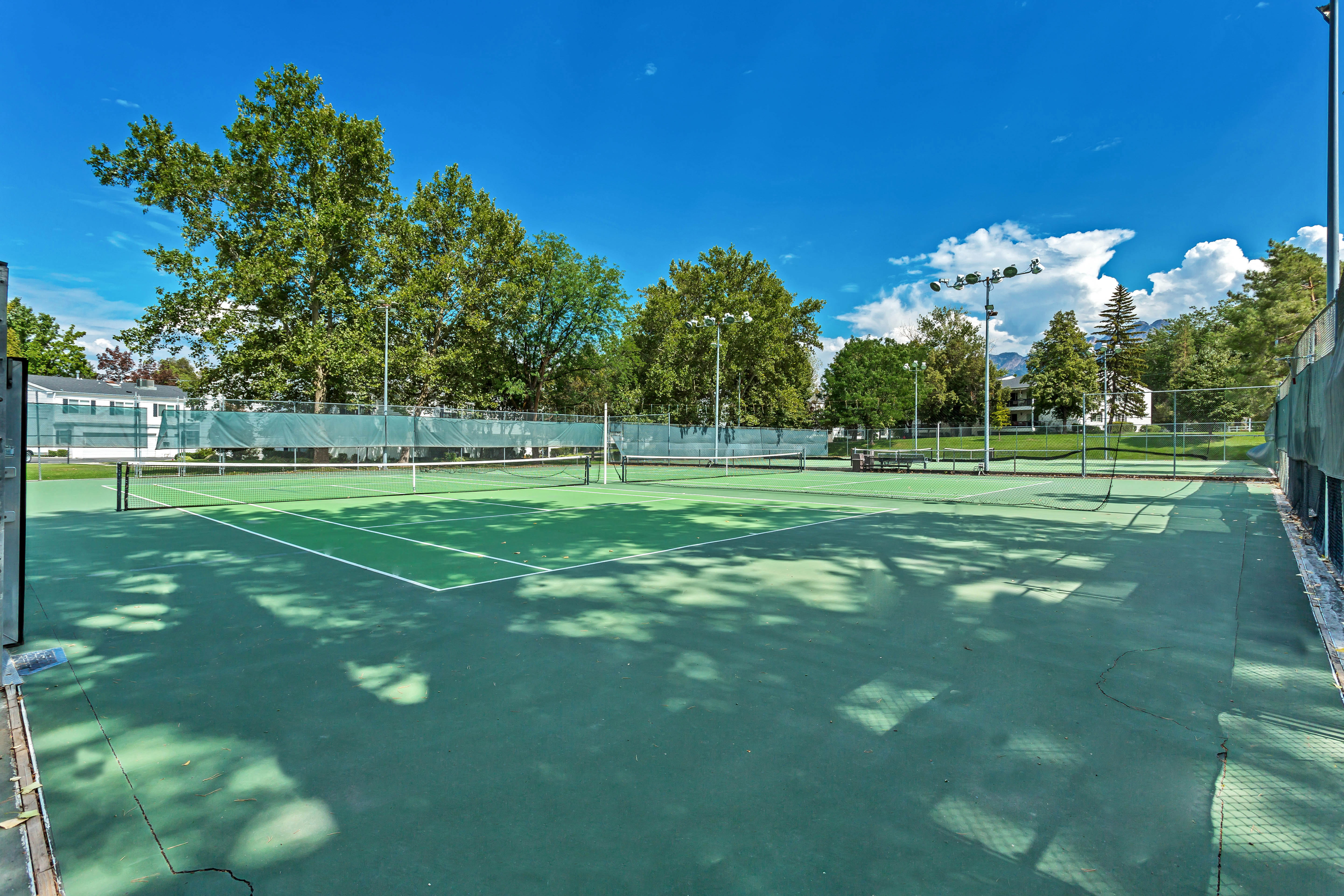 Tennis court featuring a green playing surface, perimeter fencing, and overhead lighting