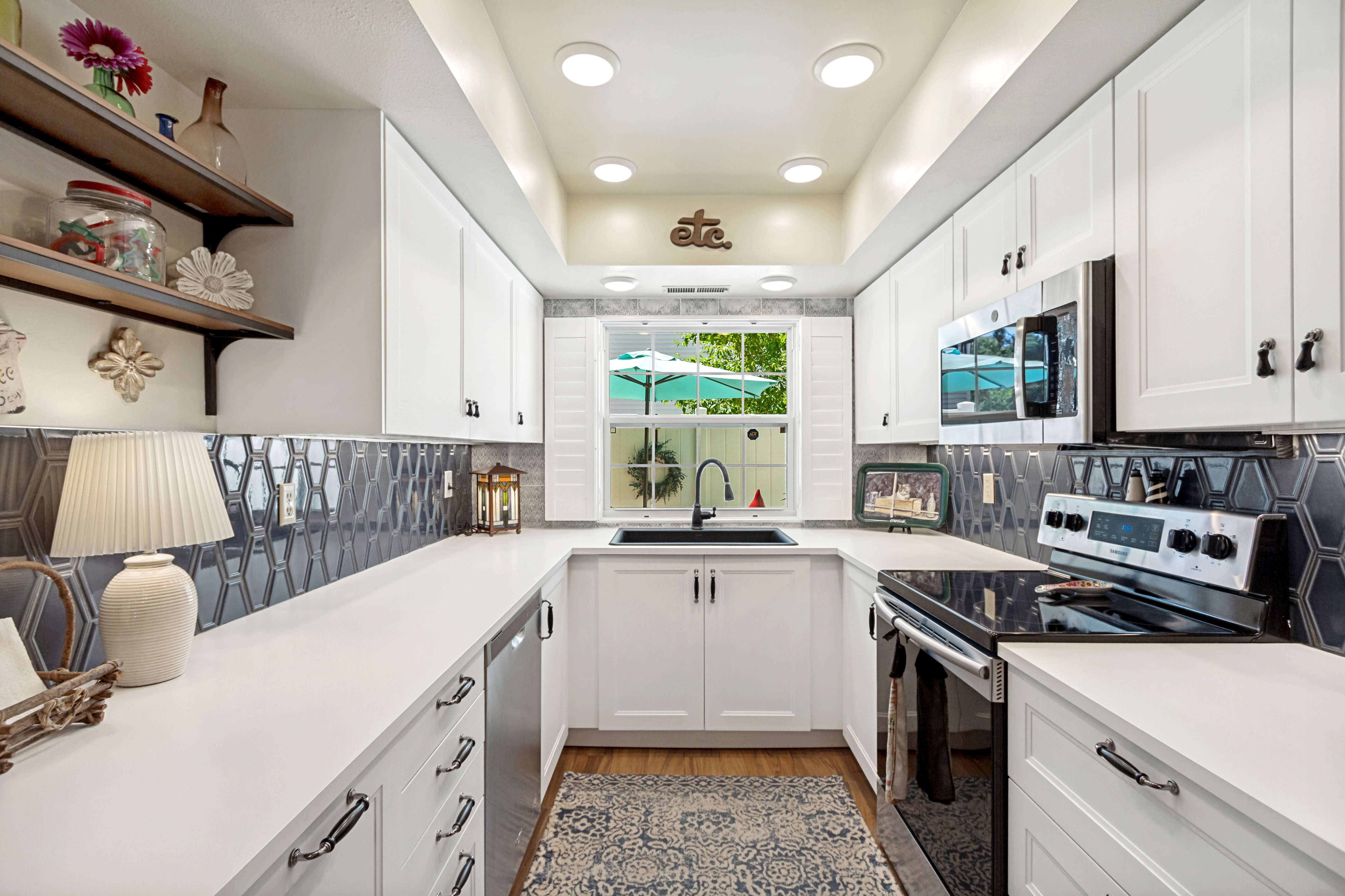 Bright kitchen featuring white cabinetry, a black hexagonal tile backsplash, stainless steel appliances, a built-in microwave, and recessed lighting