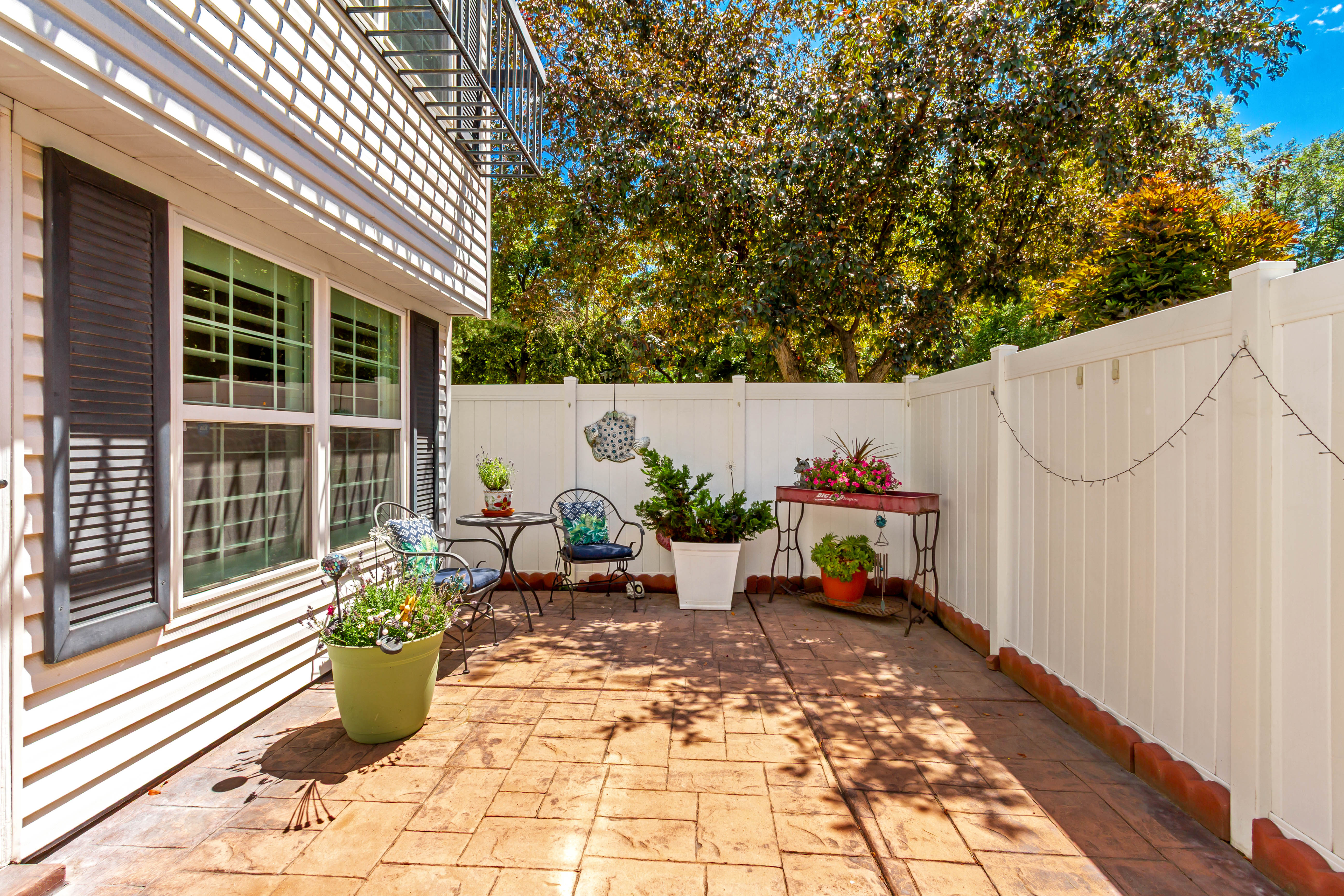 Private outdoor patio featuring stamped concrete flooring, white privacy fencing, and exterior siding with black louvered shutters