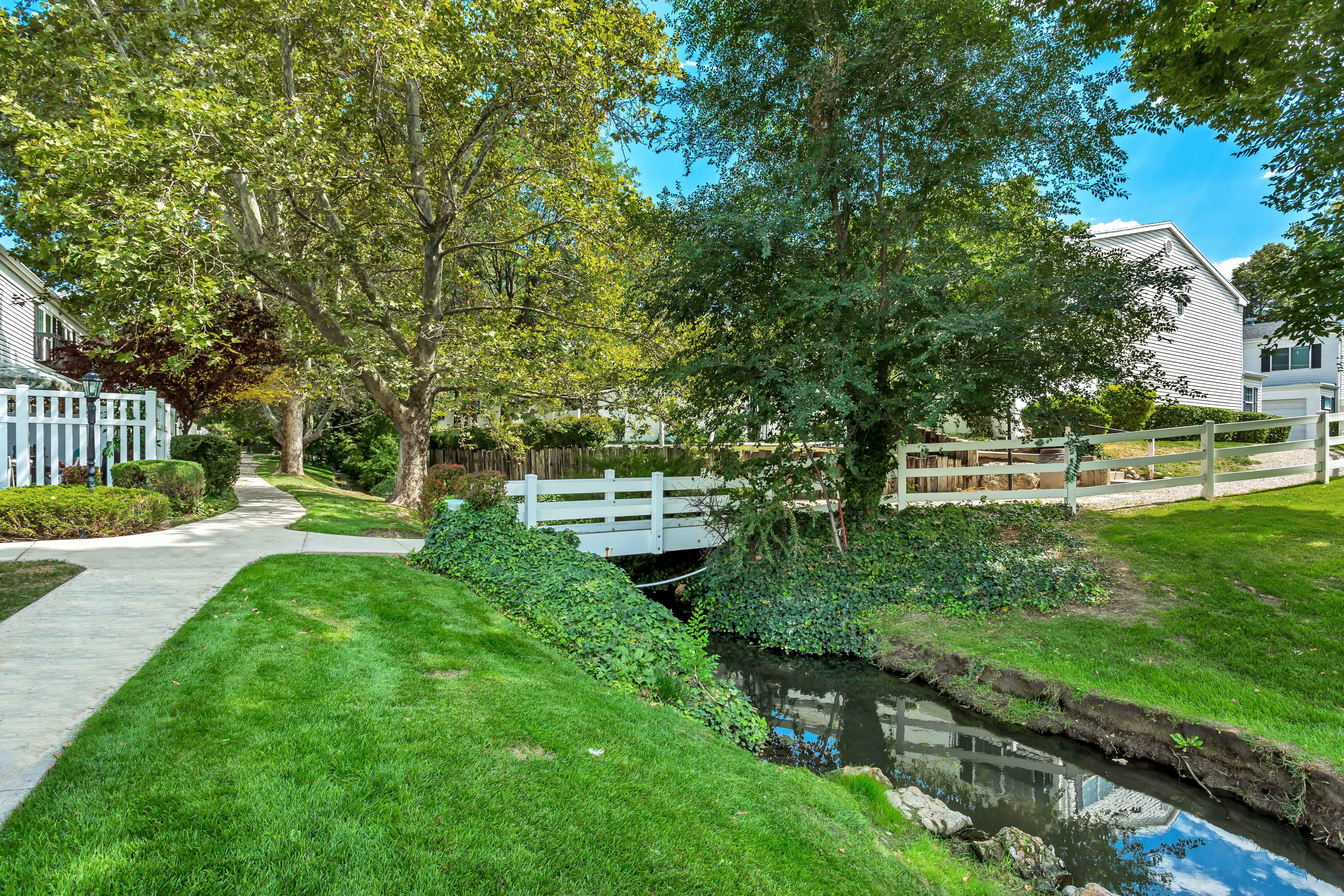 Manicured landscaping featuring a stone pathway, mature trees, and a decorative white bridge over a stream