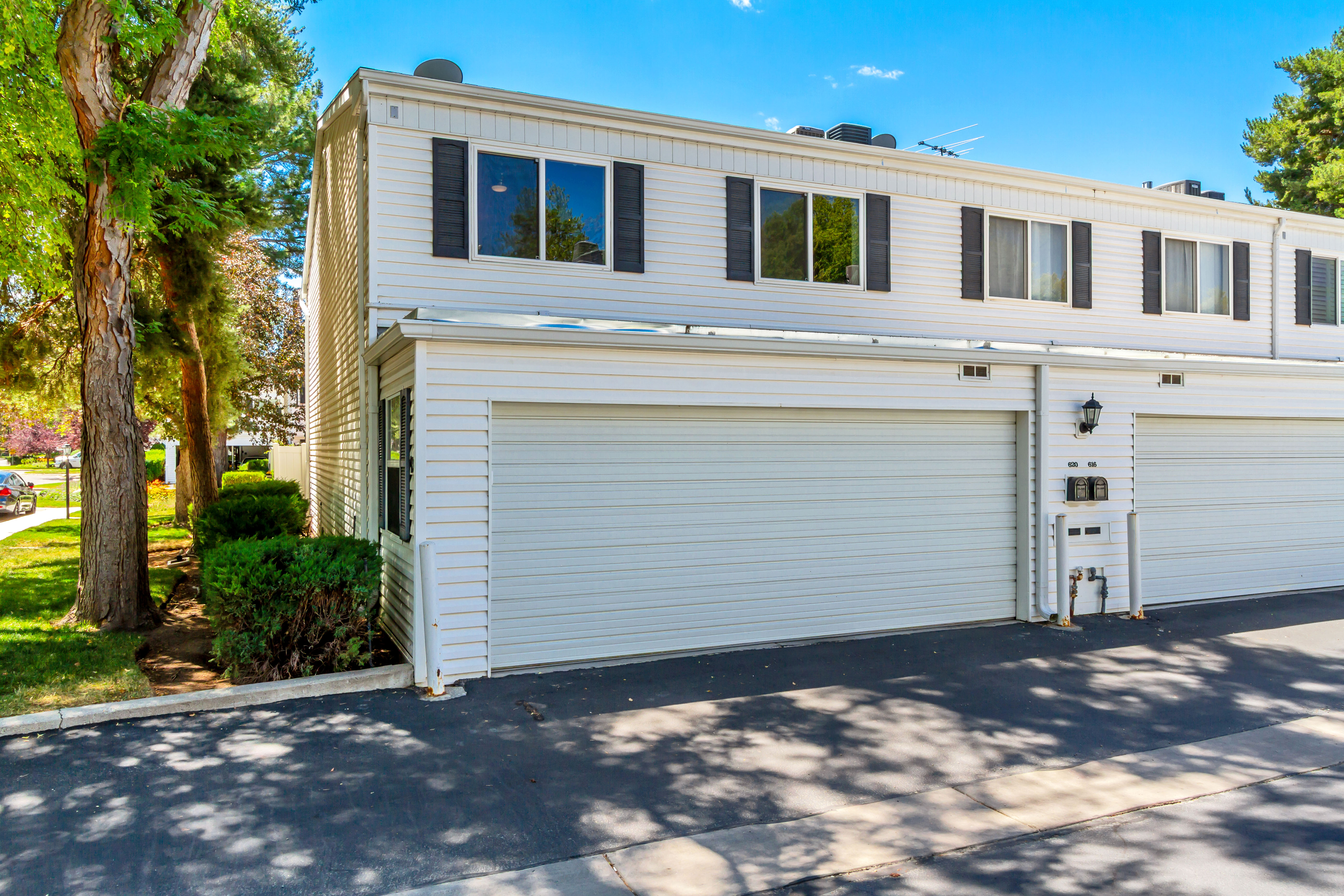 White siding exterior featuring two garage doors, second-story windows with dark shutters, and established perimeter landscaping