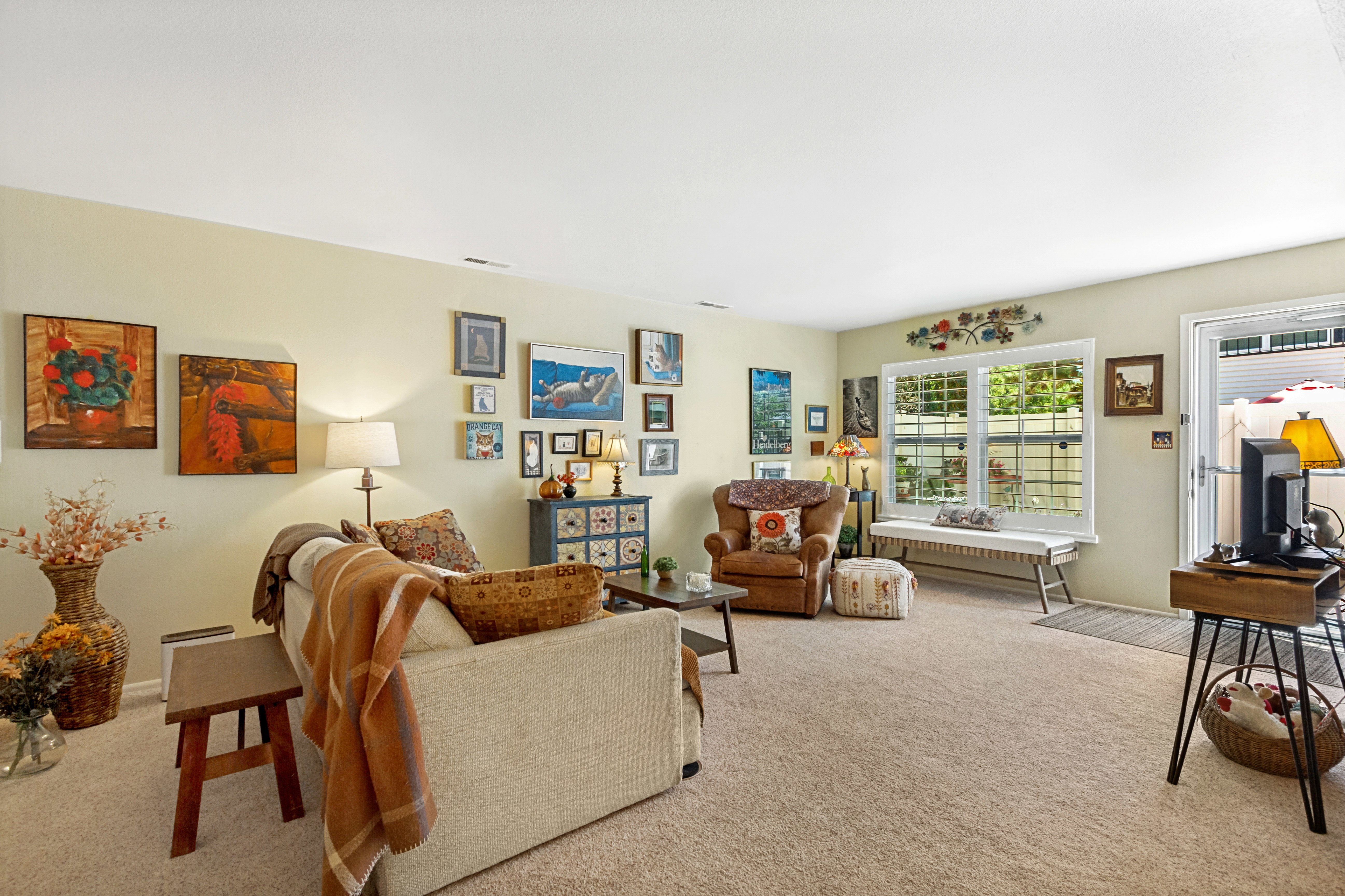 Carpeted living area featuring a large window with plantation shutters, a light-colored wall finish, and a glass-paneled exterior door