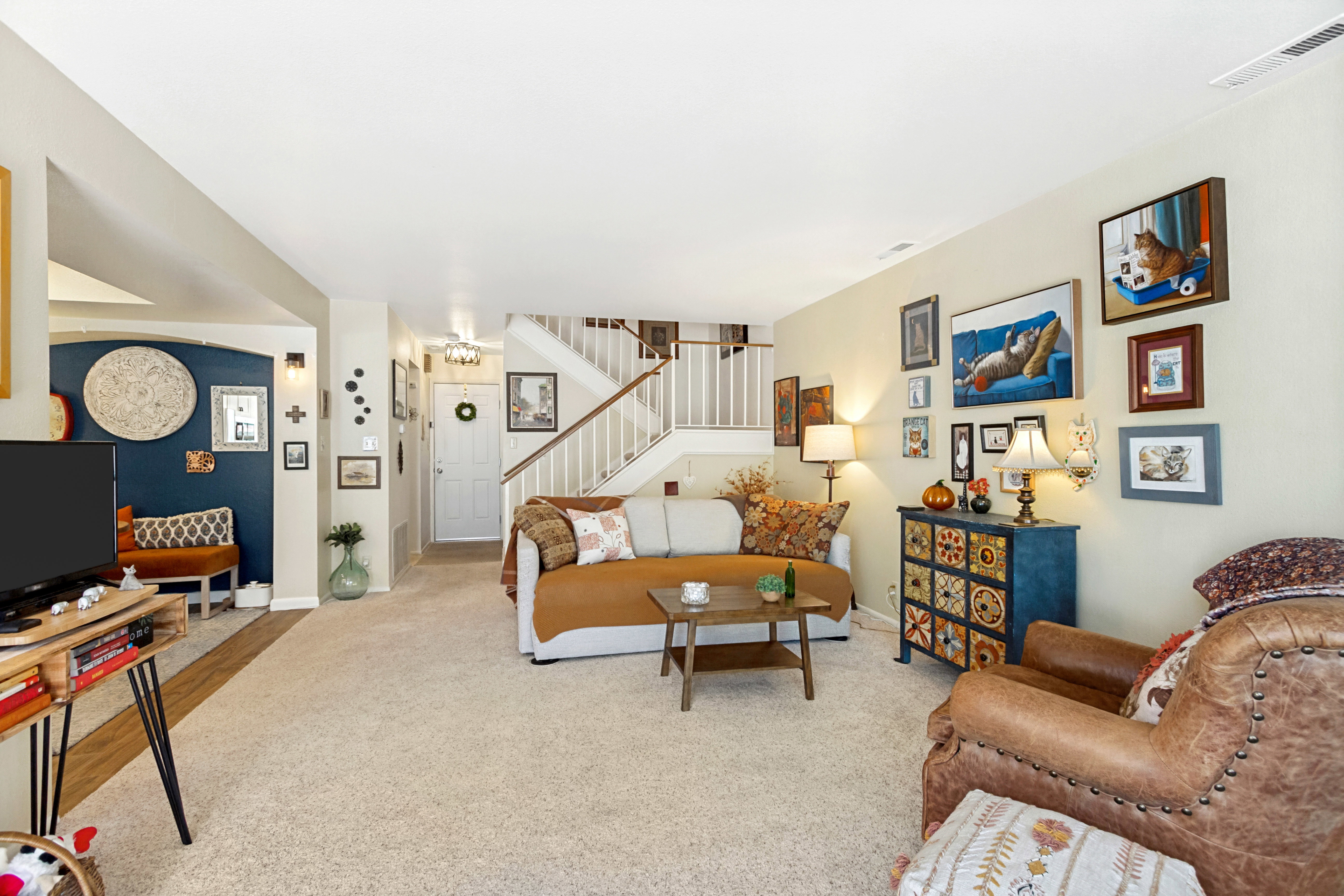 Spacious living area featuring neutral carpeting, a staircase with white risers and wood-finish handrails, and an arched entryway with contrasting wall color