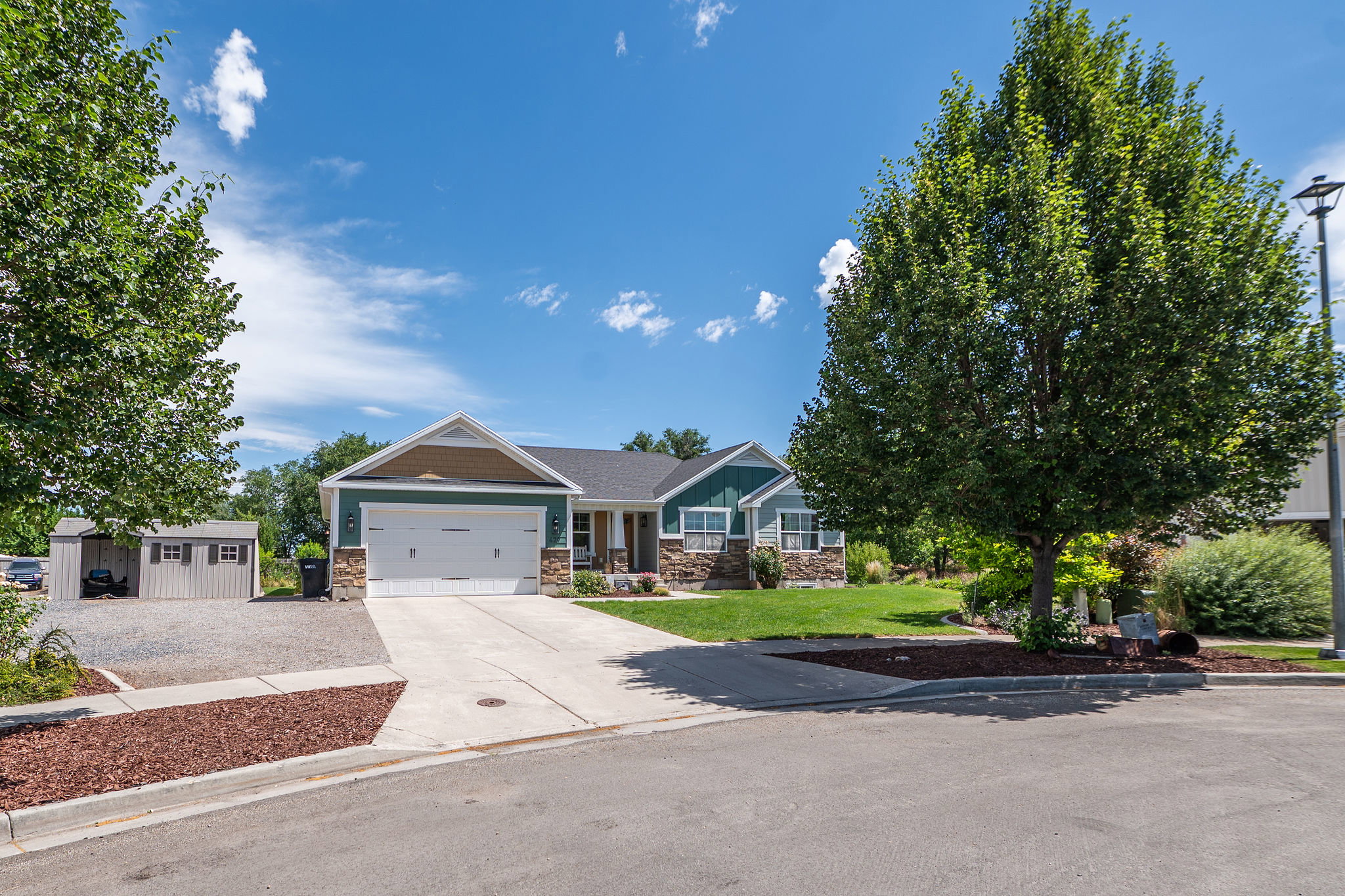 Modern ranch-style residence featuring a two-car garage, stone and siding exterior accents, a covered front porch, and mature trees