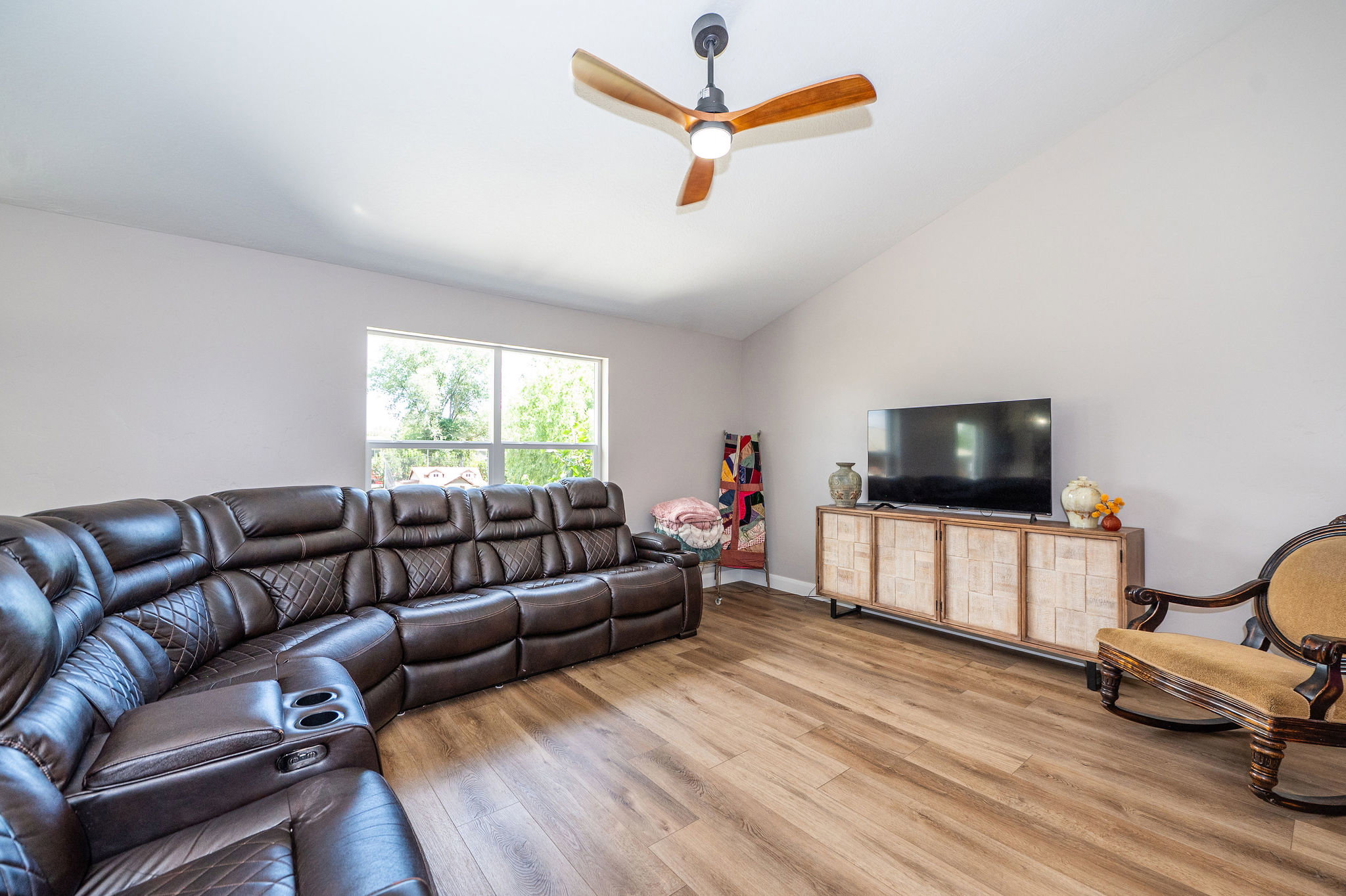 Living area featuring vaulted ceilings, wood-finish flooring, and a contemporary ceiling fan with integrated lighting