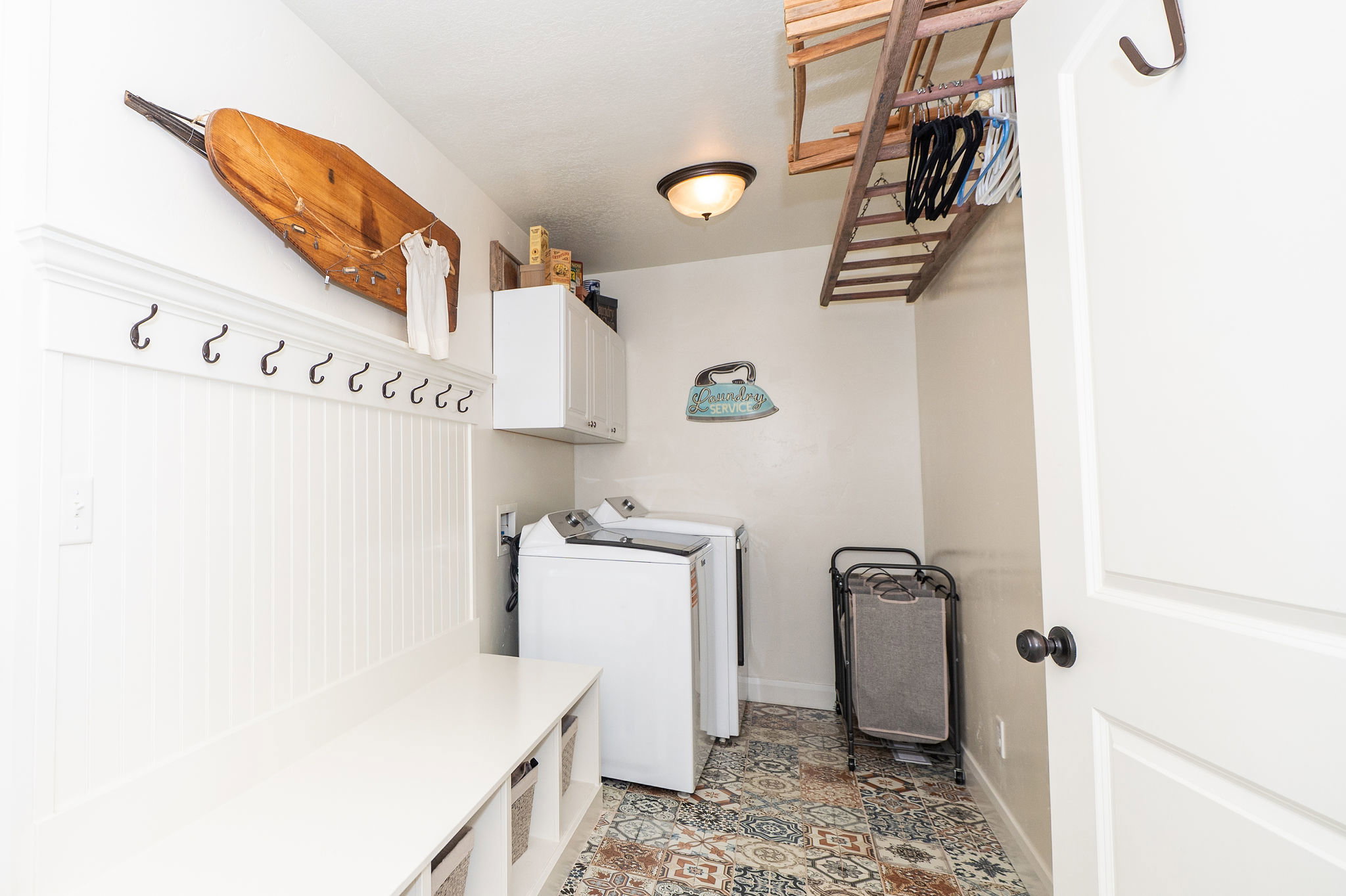 Dedicated laundry area featuring a built-in bench with storage, beadboard wall paneling, and an overhead clothes drying rack