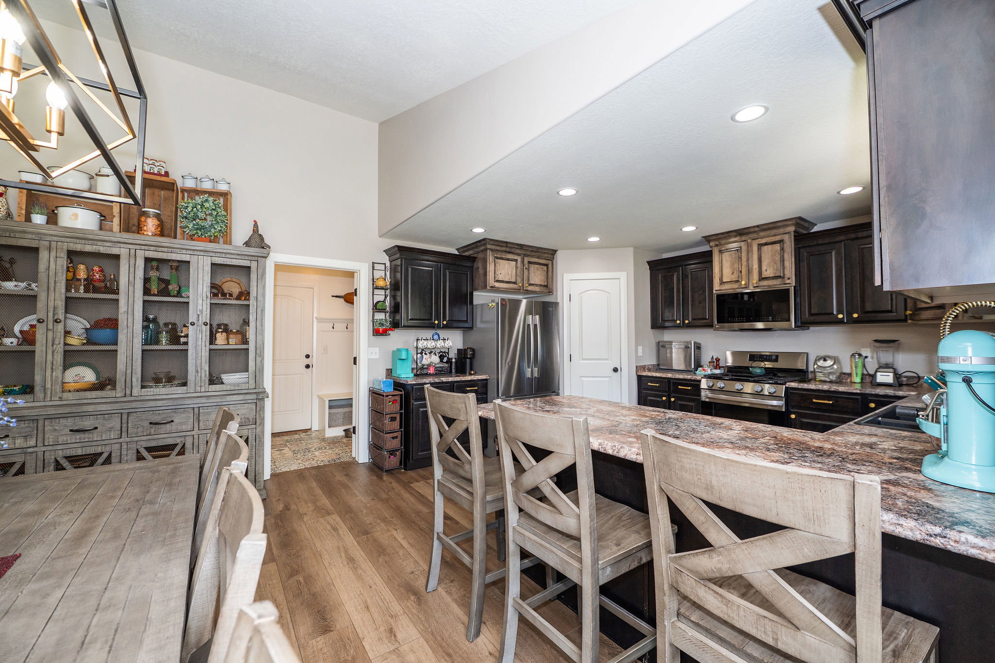 Spacious kitchen with a large island featuring a stone countertop, dark cabinetry, stainless steel appliances, and wood-finish flooring