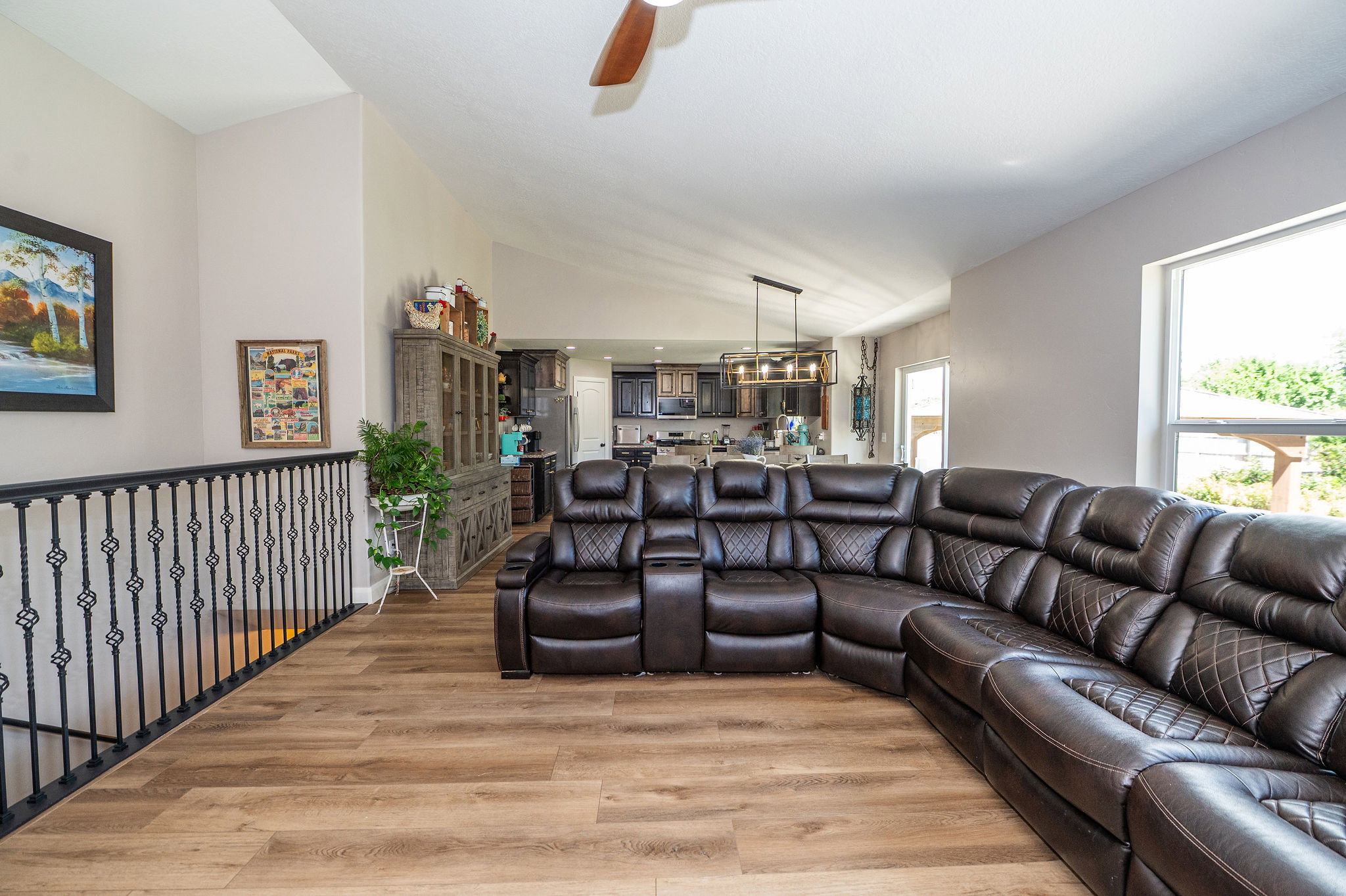 Spacious open-concept living area featuring vaulted ceilings, wood-finish flooring, and a decorative wrought iron railing
