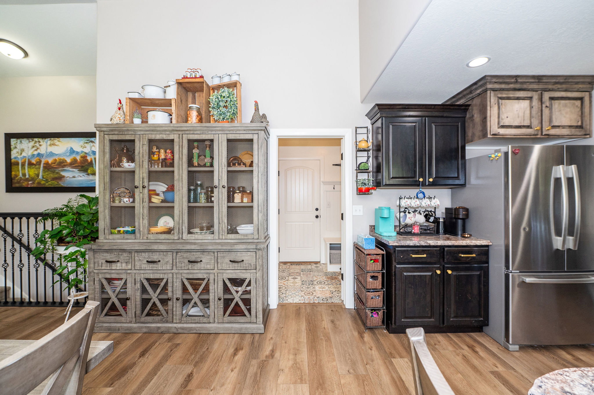 Open-concept interior featuring wood-finish flooring, a kitchen area with dark cabinetry, stainless steel refrigerator, and recessed lighting