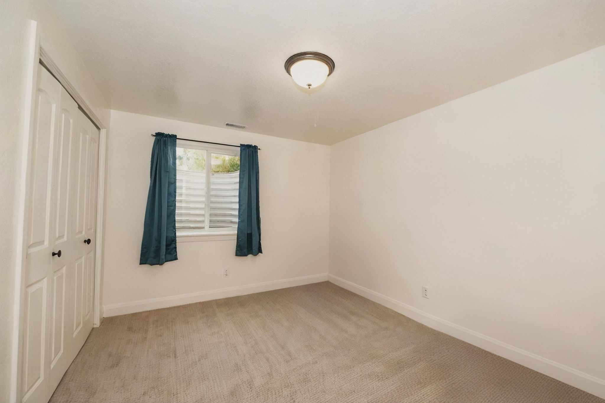 Neutral-toned interior room featuring light carpet flooring, white walls, and a window with a window well