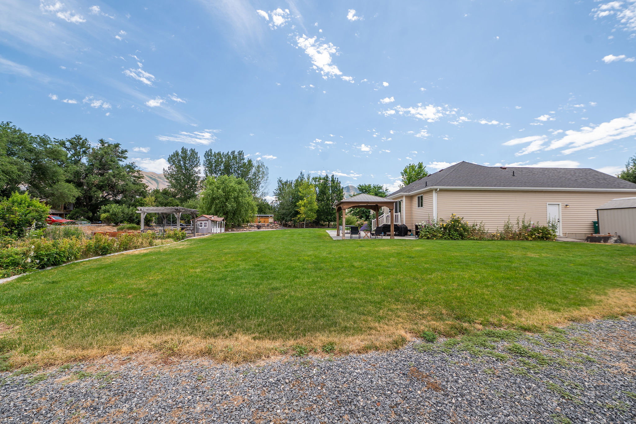Expansive backyard featuring a large green lawn, mature trees, and landscaping