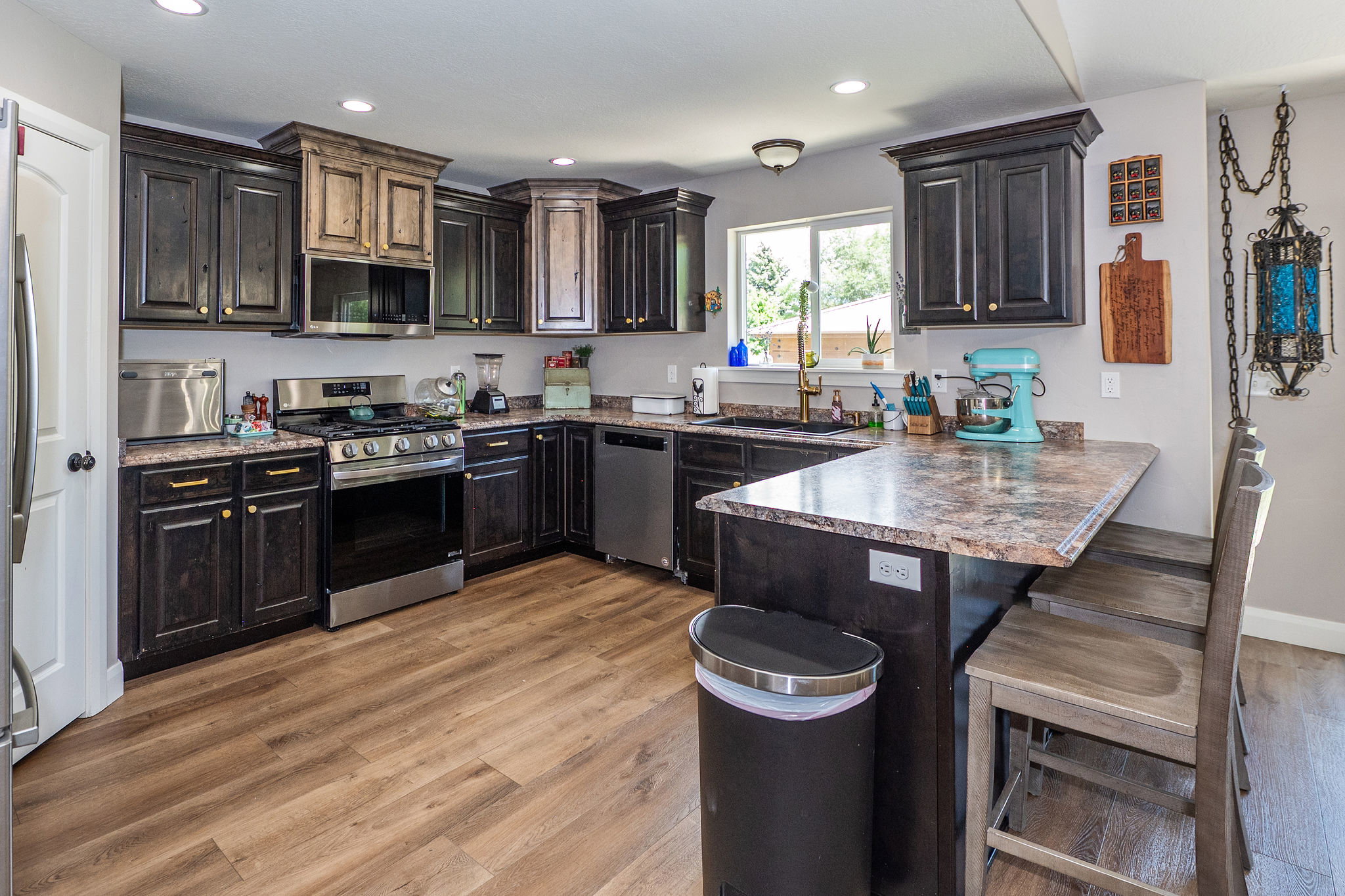 Kitchen featuring wood-finish flooring, dark wood cabinetry, a stainless steel gas range, and a breakfast bar with stone-look countertops