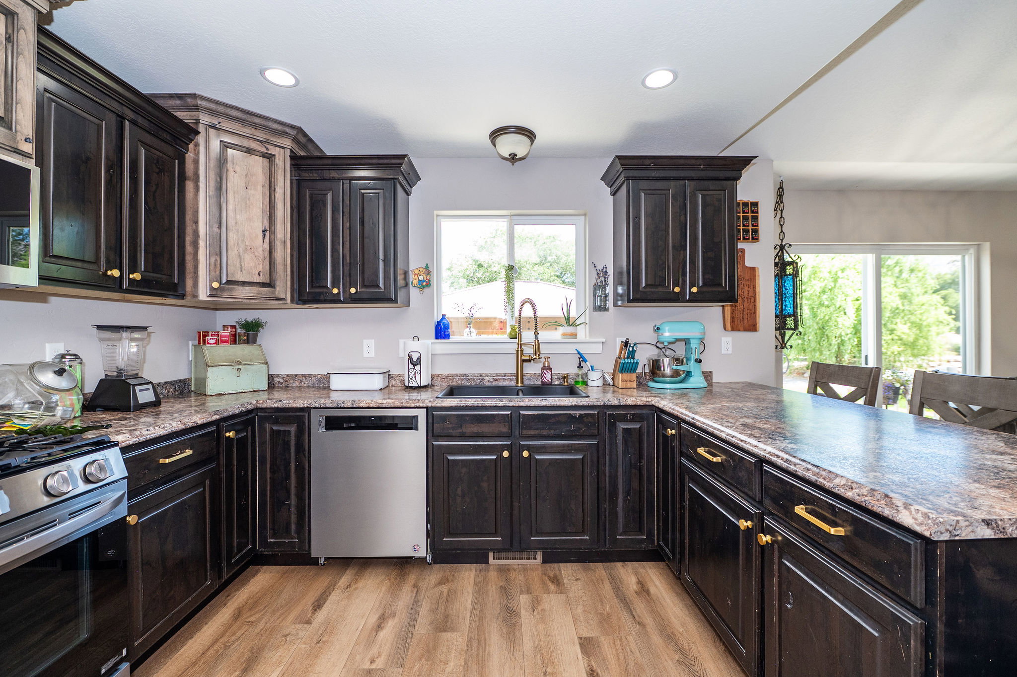 Kitchen featuring dark-toned cabinetry, wood-finish flooring, a stainless steel dishwasher, a built-in oven with a gas range, and a spacious countertop