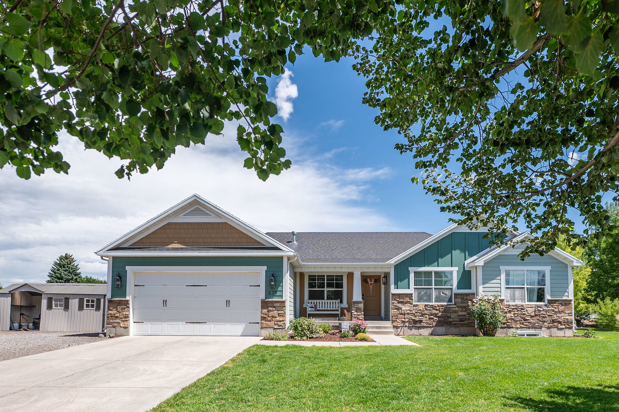Ranch-style residence featuring a two-car garage, stone and siding exterior, front porch with a swing, and a manicured lawn
