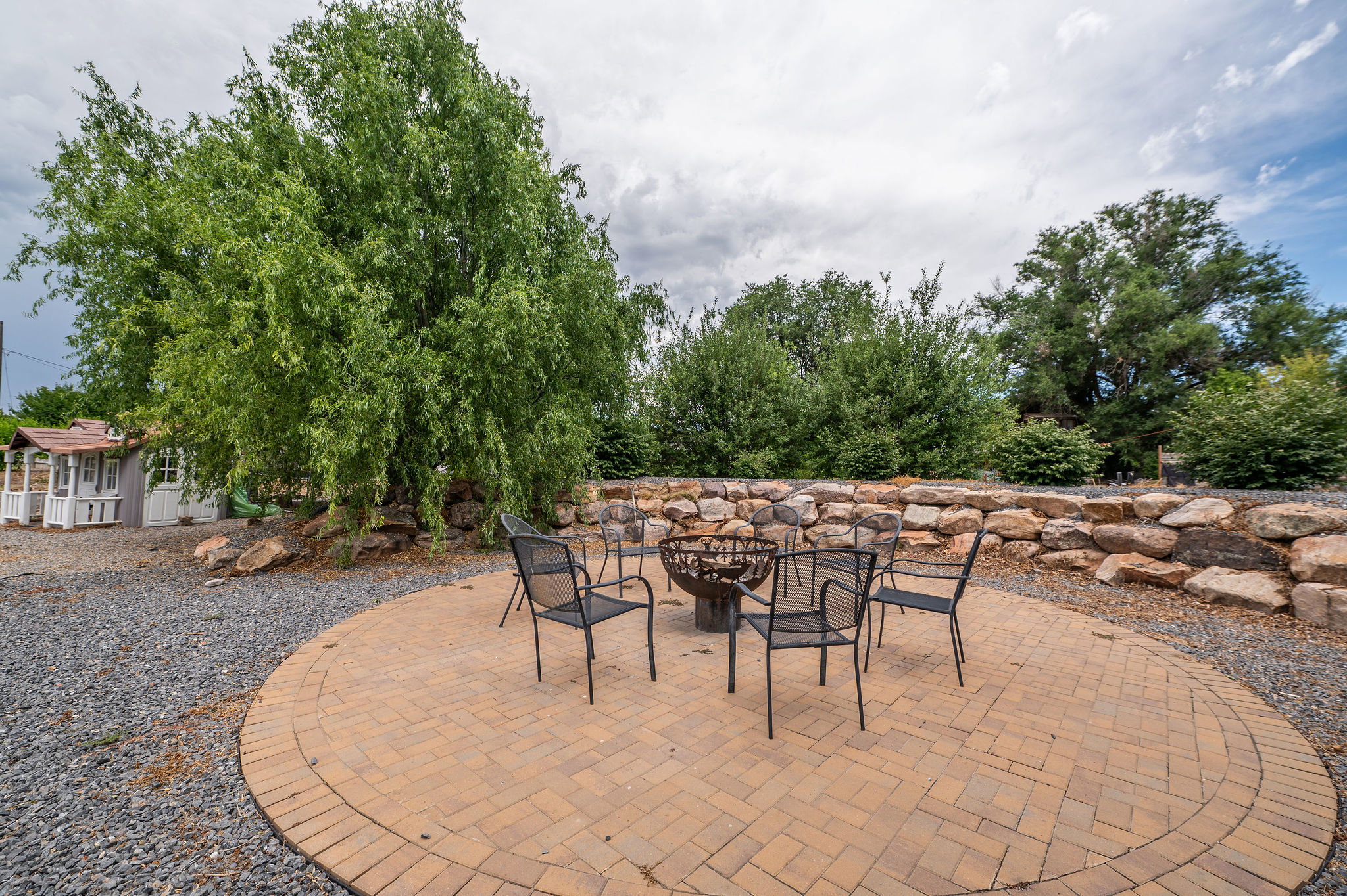 Circular paver patio with a central fire pit, surrounded by a stone retaining wall and mature trees