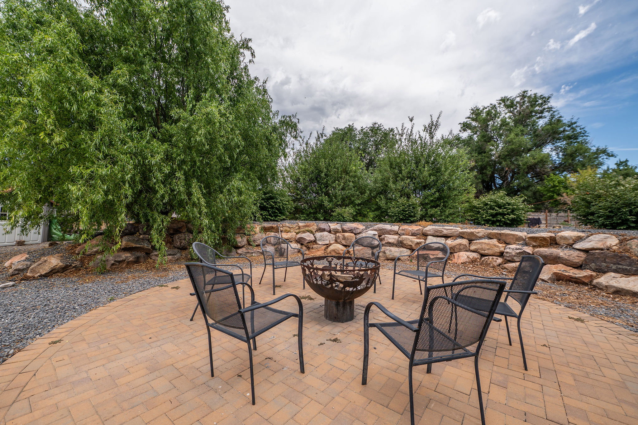 Brick paver patio with built-in fire pit, surrounded by a natural stone retaining wall and mature trees