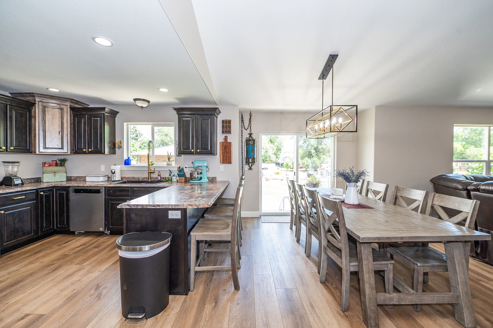 Open-concept kitchen and dining area featuring wood-finish flooring, dark wood cabinetry with gold-toned hardware, and a center island with countertop seating