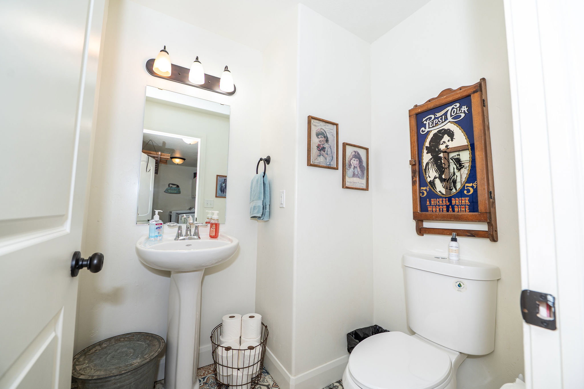 Pedestal sink with chrome faucet, wall-mounted mirror, and three-light vanity fixture