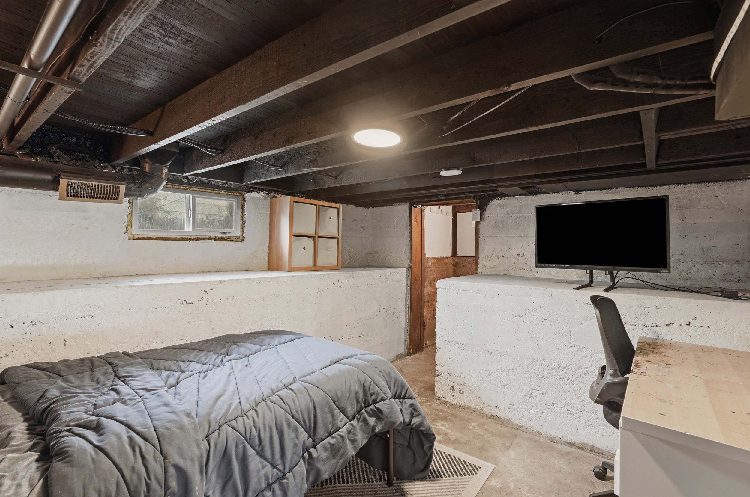 Basement space featuring exposed ceiling joists, concrete walls, and a recessed ceiling light.