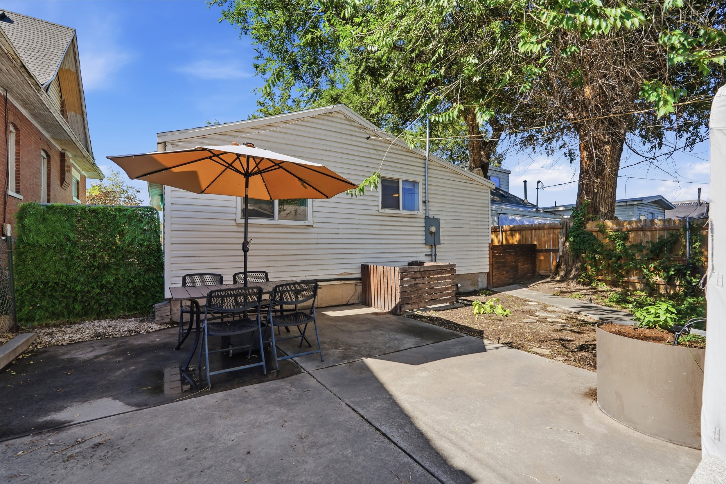 Concrete patio space featuring a privacy hedge, mature trees, and a wooden fence