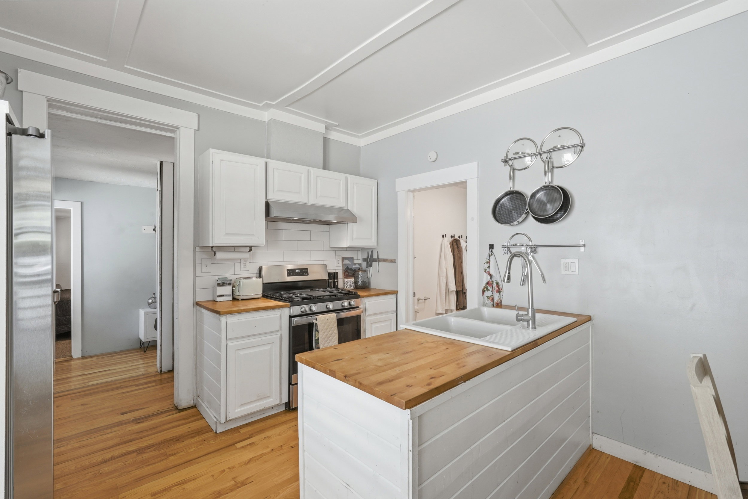 Kitchen featuring white shaker cabinetry, subway tile backsplash, stainless steel gas range, a central island with a wood-finish countertop and integrated double-basin sink, and wood-finish flooring