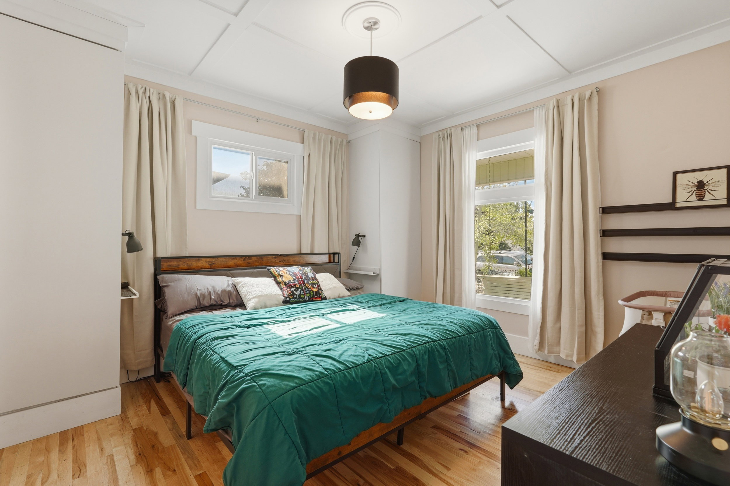Owners suite off living room, featuring wood-finish flooring, built in closet, two windows with white trim, and a white coffered ceiling.