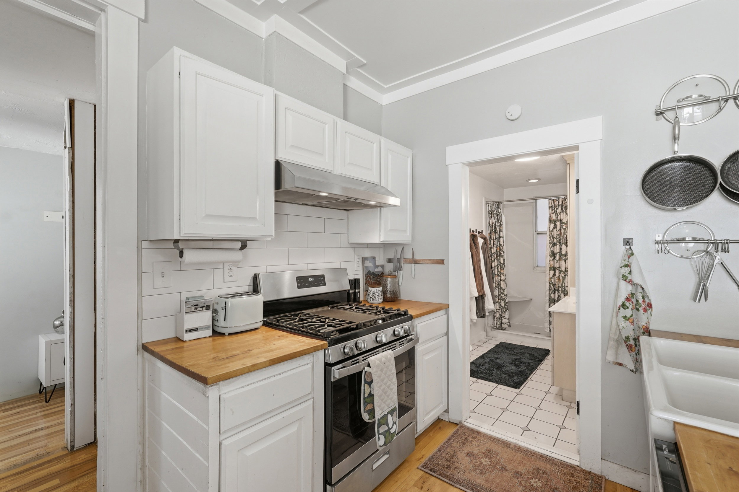 Kitchen featuring white cabinetry, wood-finish countertops, subway tile backsplash, and a stainless steel gas range with a matching range hood