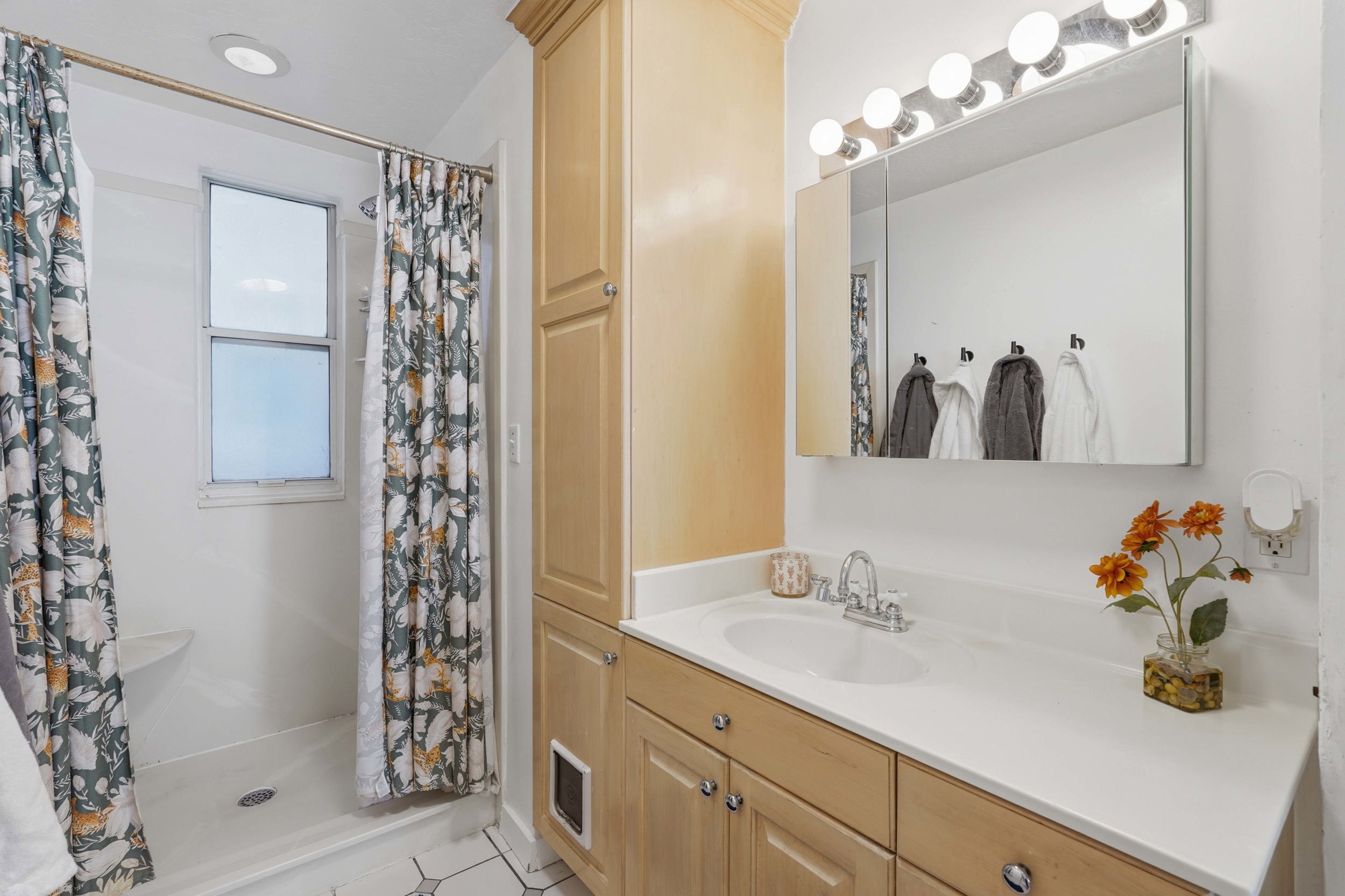 Bathroom off kitchen, featuring a vanity with an integrated sink, shower, and a large wall-mounted mirror and built in cabinets.