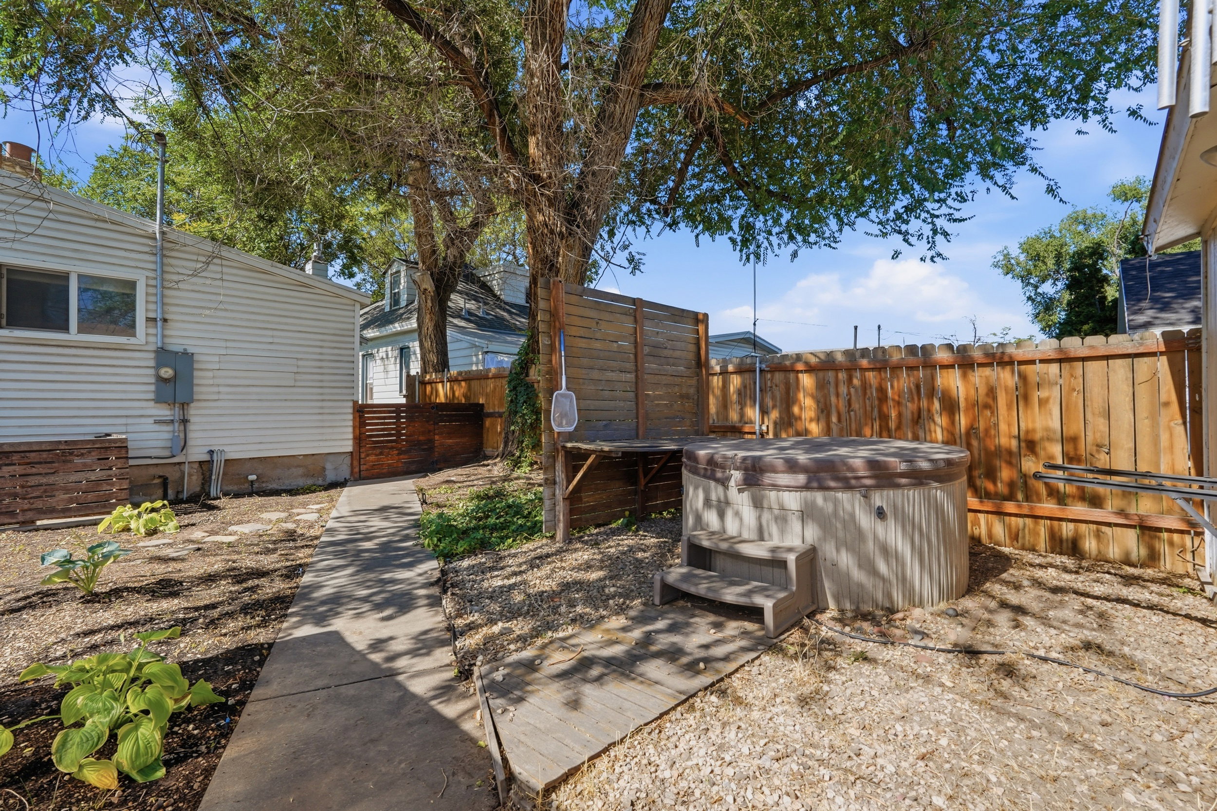 Outdoor spa with integrated steps, surrounded by a wood privacy fence and mature trees