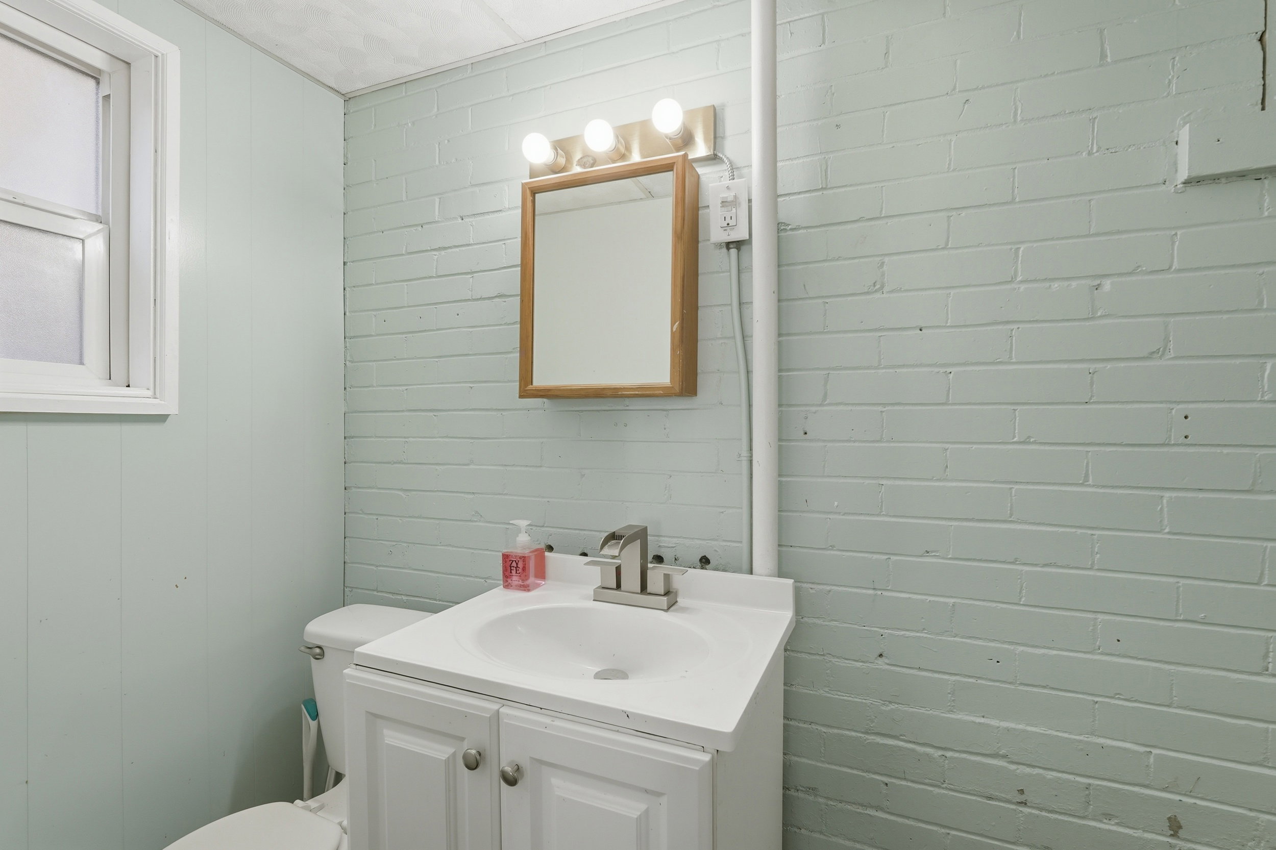 Powder Bath within Bedroom #3, featuring a white vanity with integrated sink, brushed nickel faucet, and a wall-mounted mirror with a wood-finish frame.