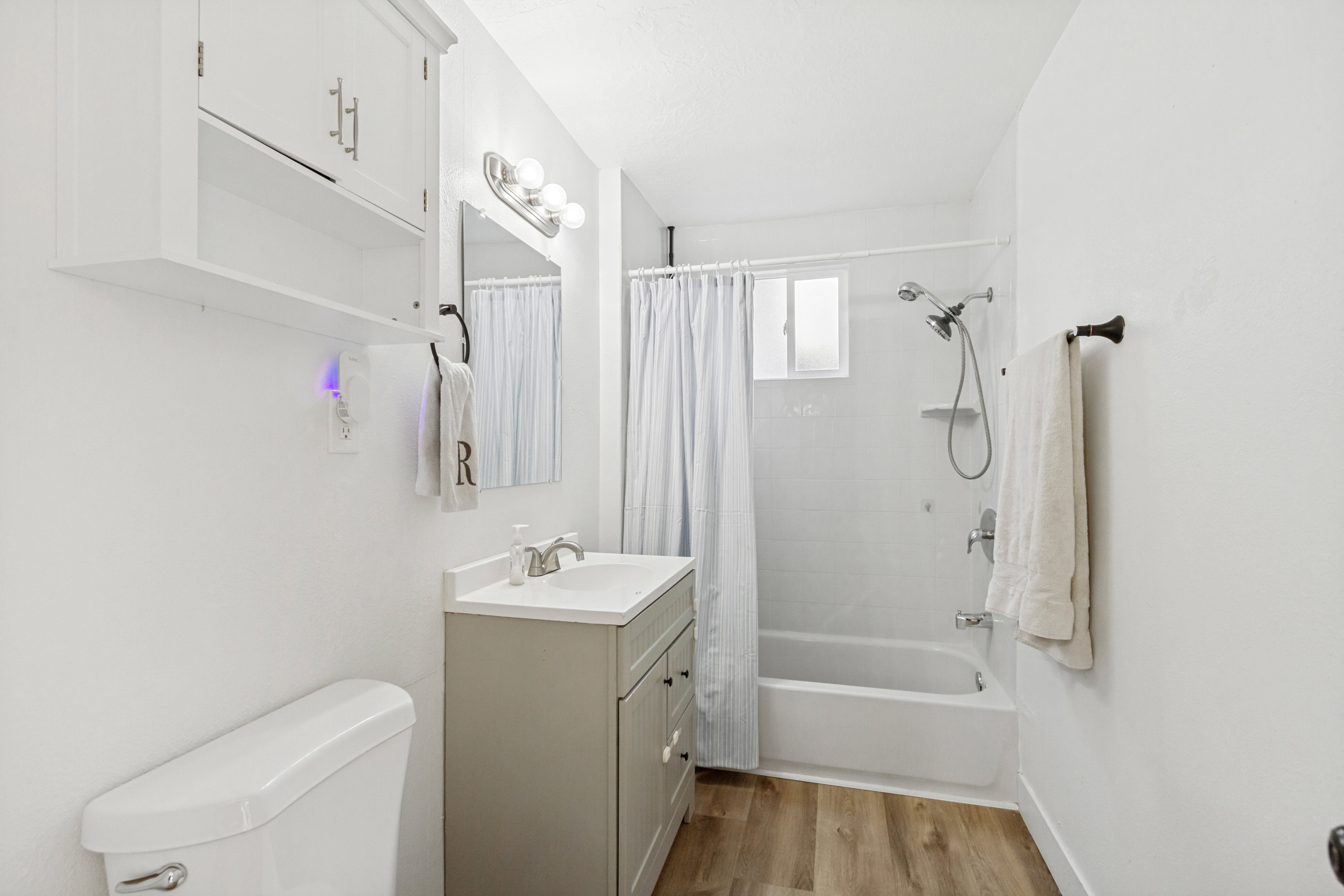 Full bathroom featuring a single vanity with a white countertop, laminate, white built-in wall cabinet, and a shower-over-tub combination with a window