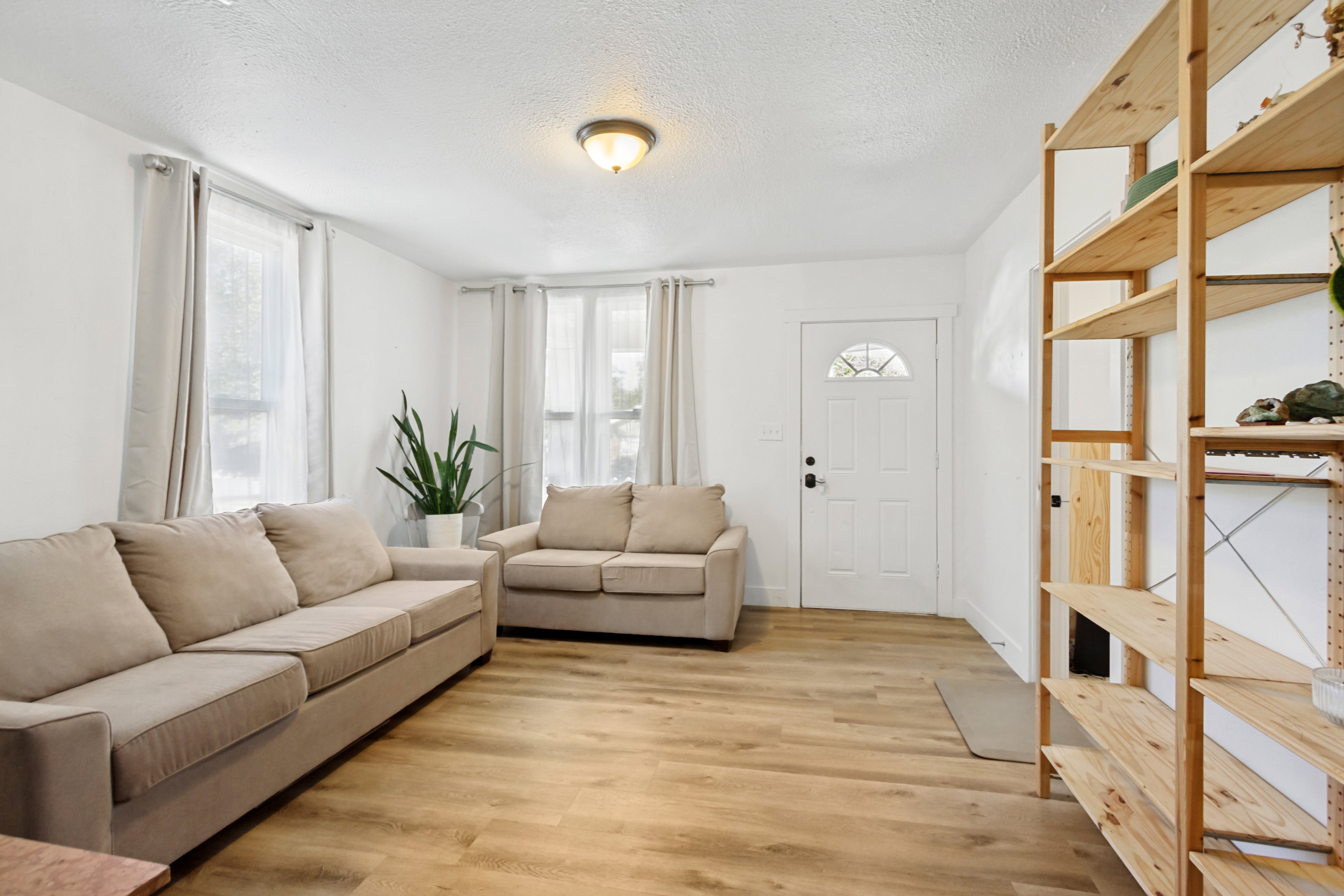 Inviting living space featuring laminate flooring, white walls, and multiple windows with curtain rods