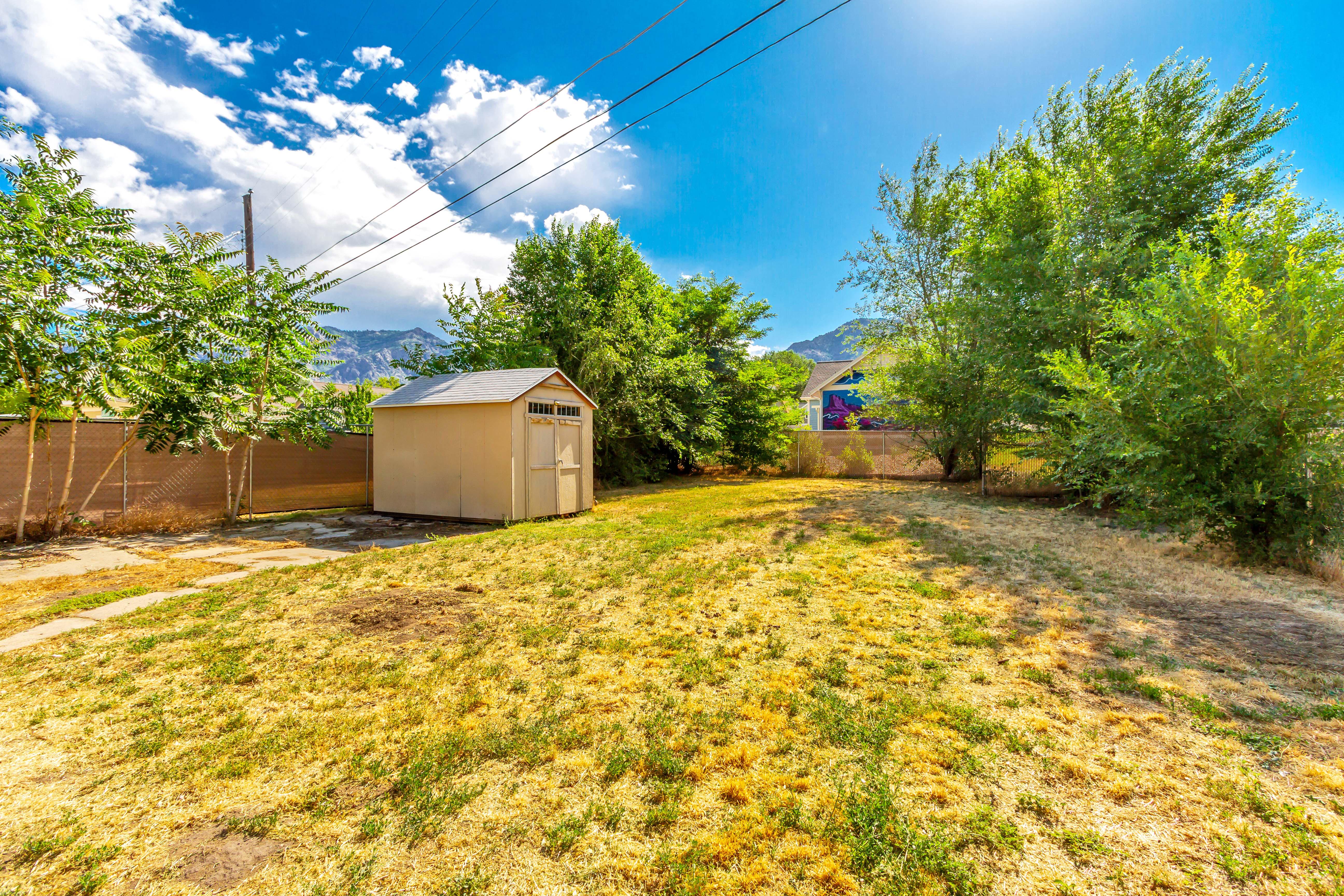 Expansive backyard featuring a detached storage shed with a gabled roof, mature trees, and perimeter fencing