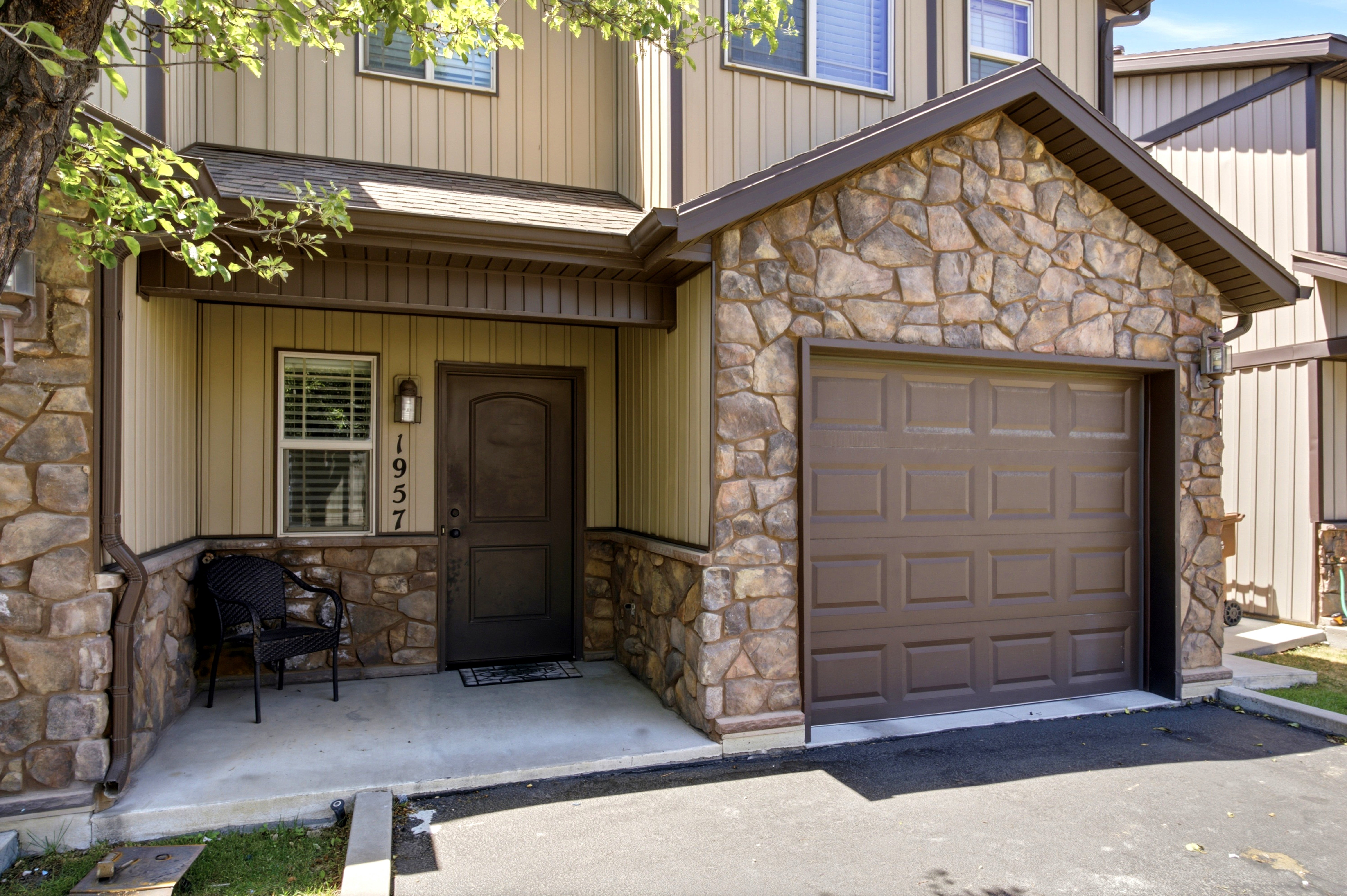Stone and siding exterior featuring an attached garage, covered entryway, and asphalt driveway