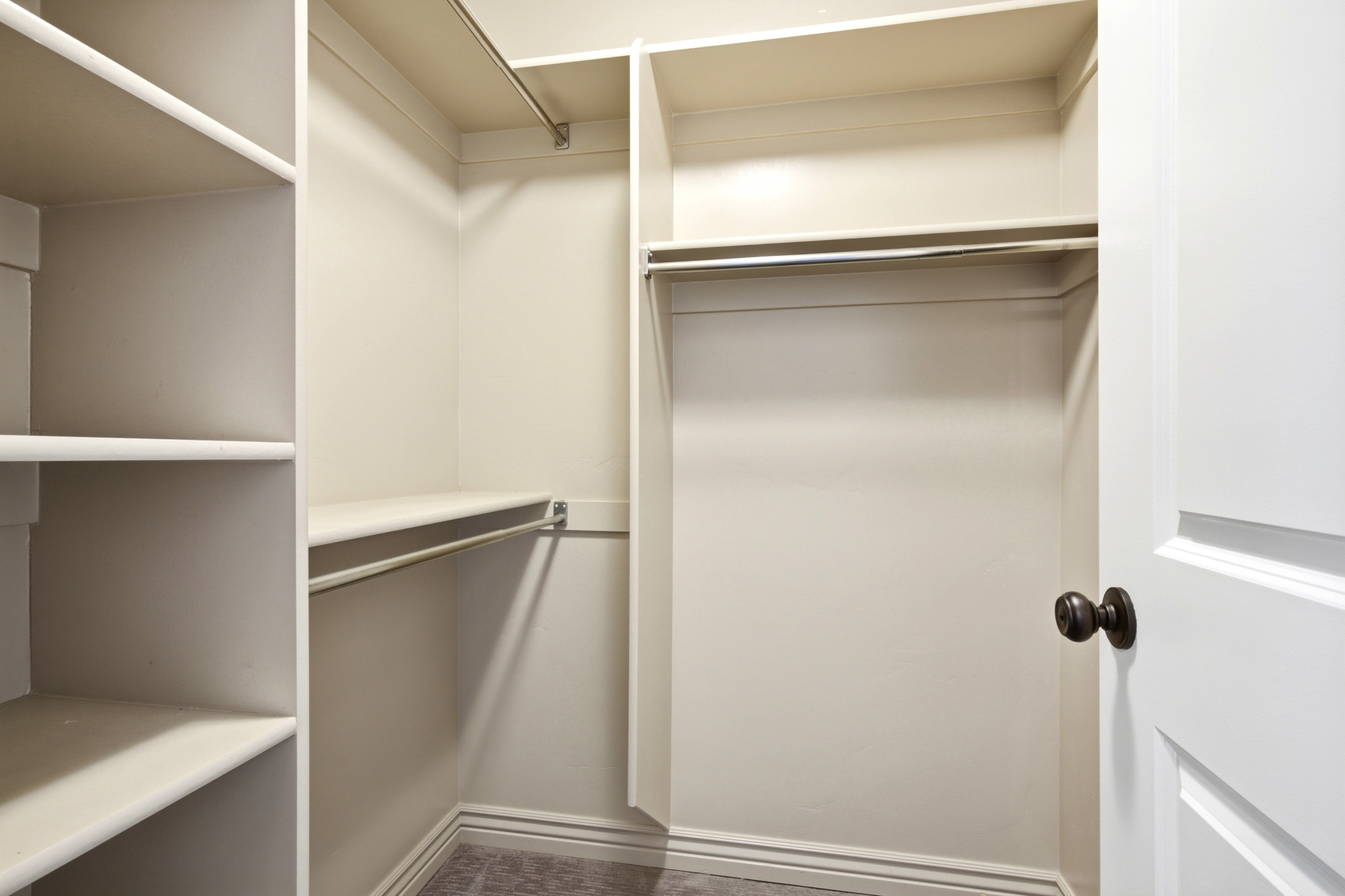 Organized closet with built-in shelving, multiple hanging rods, and carpet flooring
