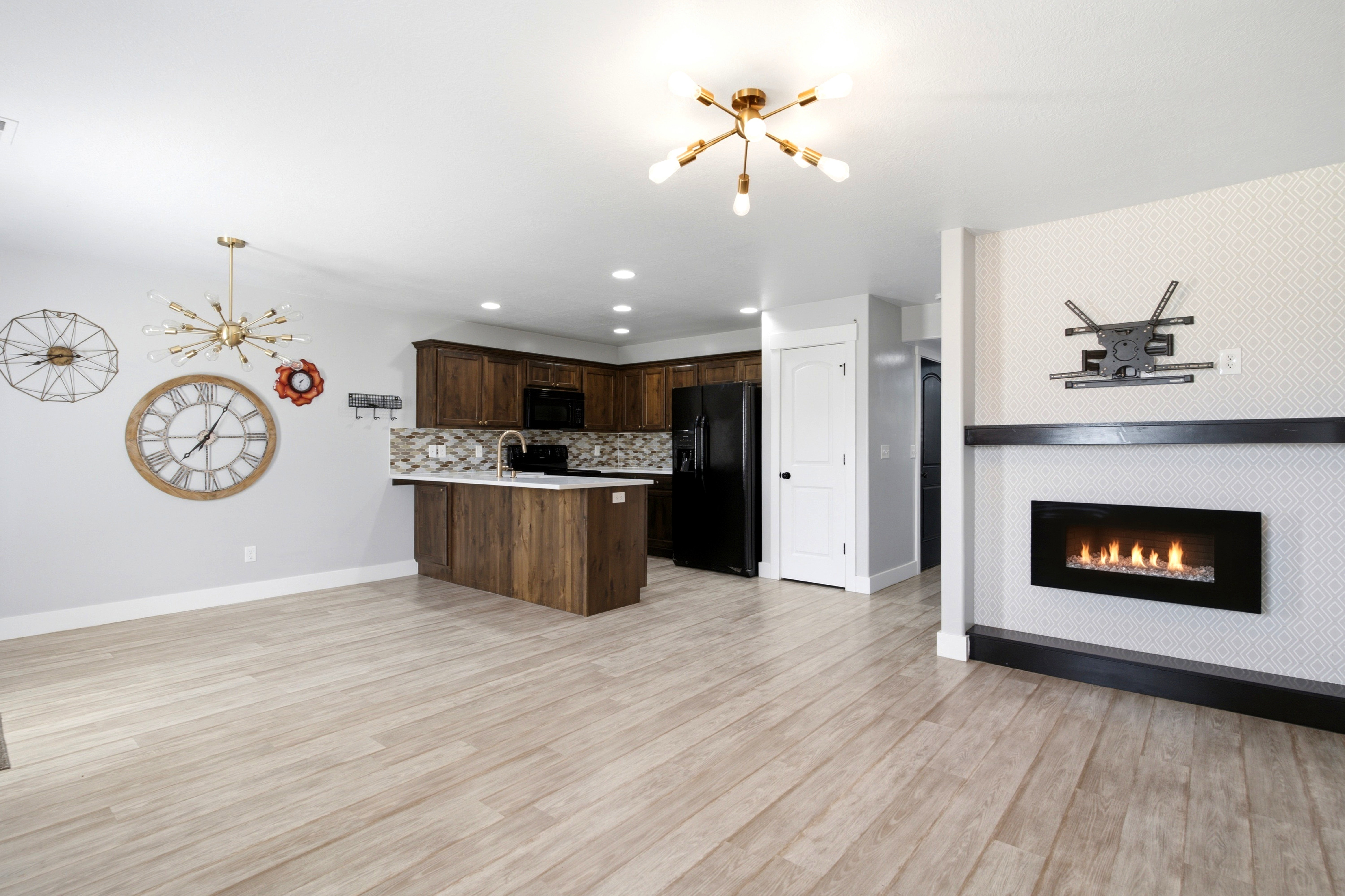 Light wood-finish flooring extending into a kitchen featuring wood cabinetry, a tile backsplash, and a breakfast bar with a sink