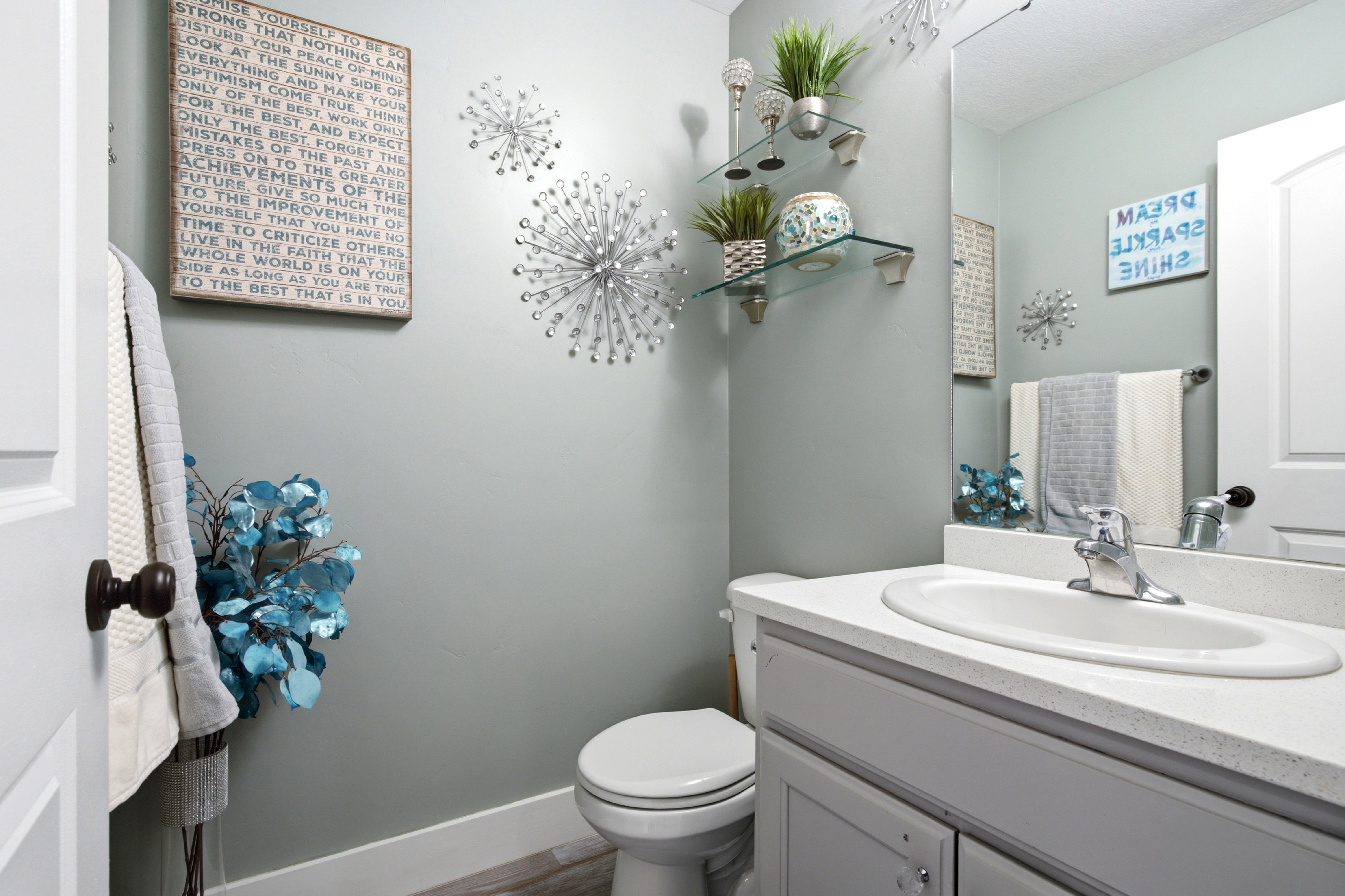 Powder room featuring a single vanity with an integrated sink, a large wall-mounted mirror, and glass shelving