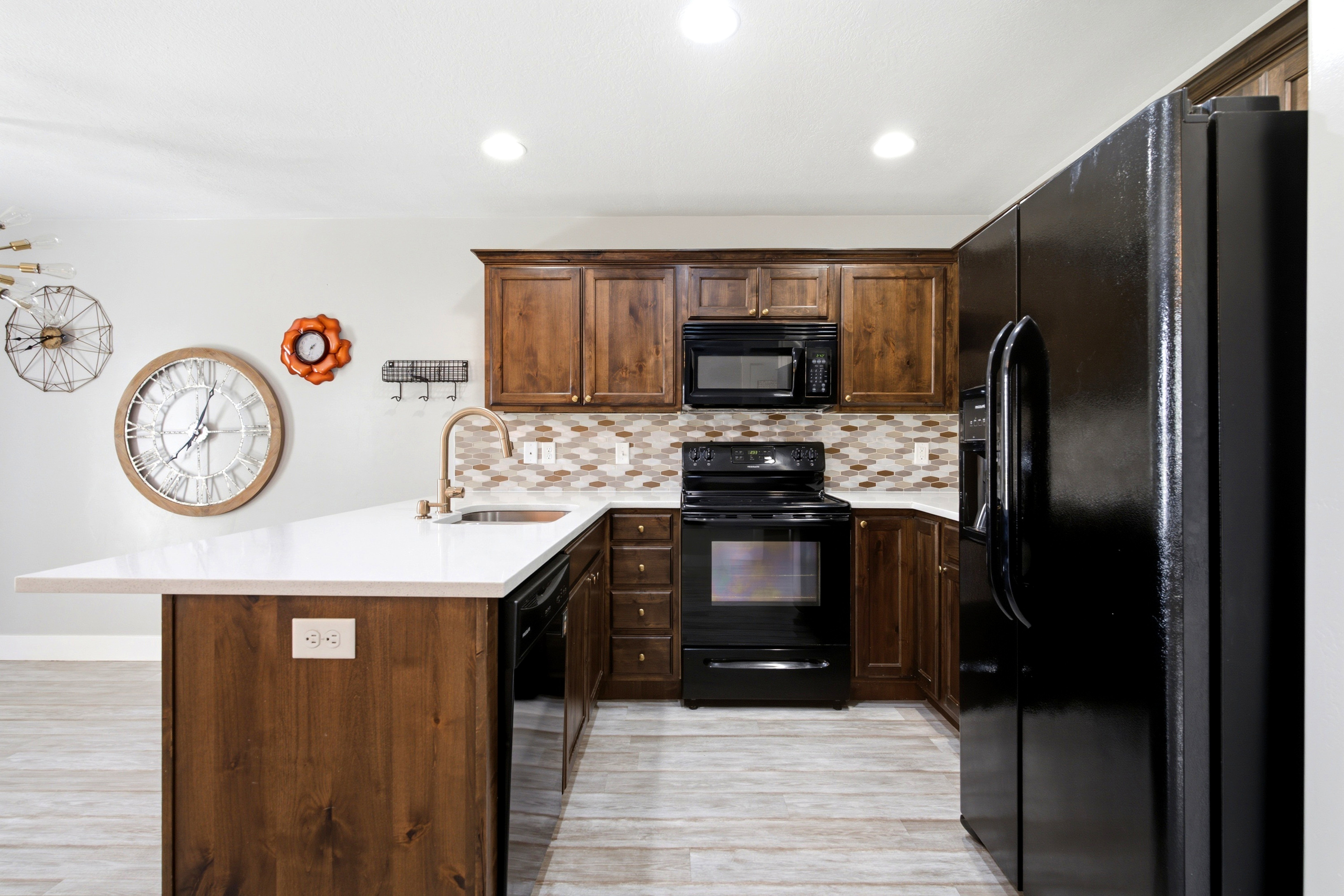 Kitchen featuring rich wood cabinetry, black appliances, a multi-tone tile backsplash, a kitchen island with a light-colored countertop, and a gooseneck faucet