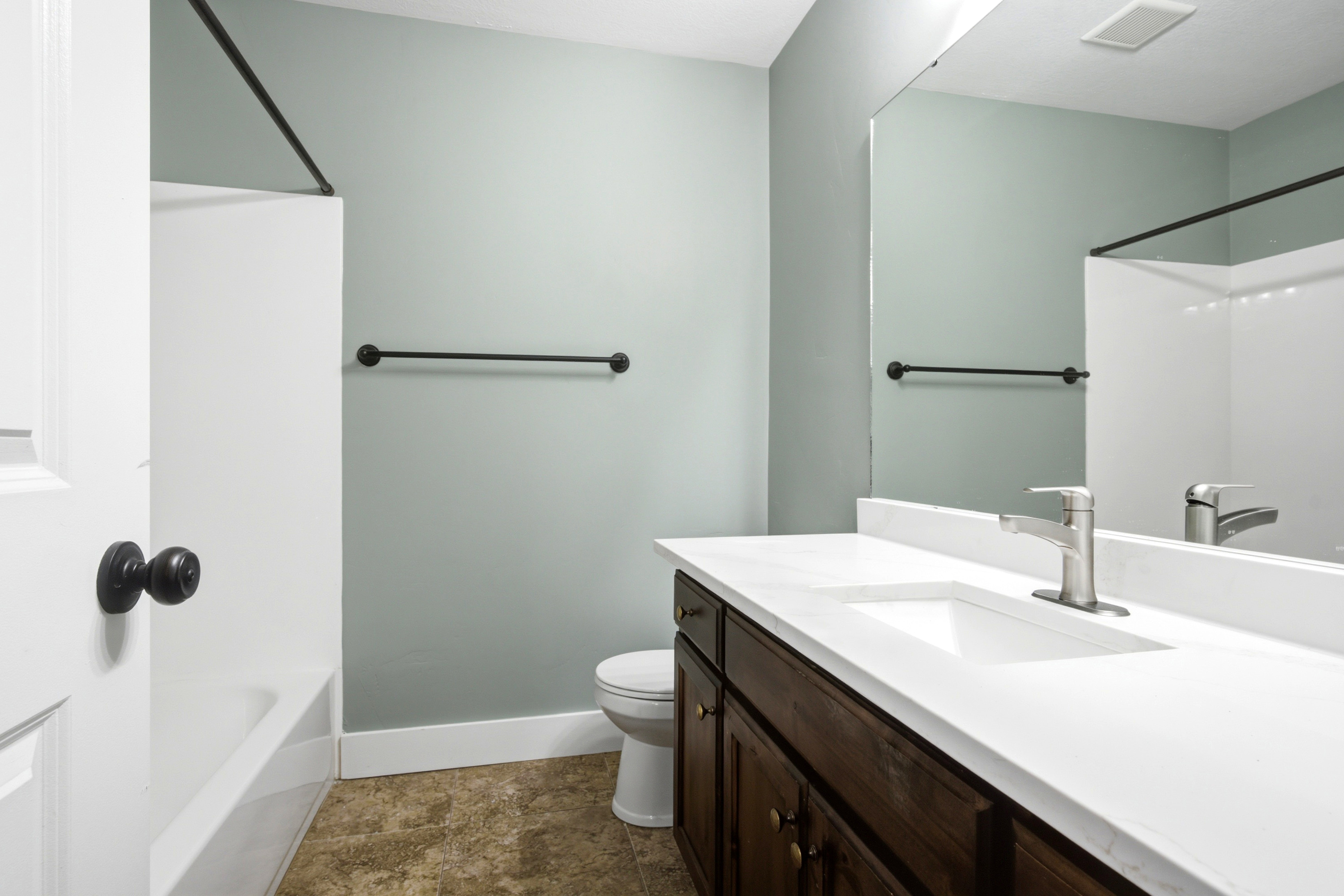 Bathroom featuring a dark wood-finish vanity with a white countertop and integrated sink, a brushed nickel faucet, and a large wall-mounted mirror